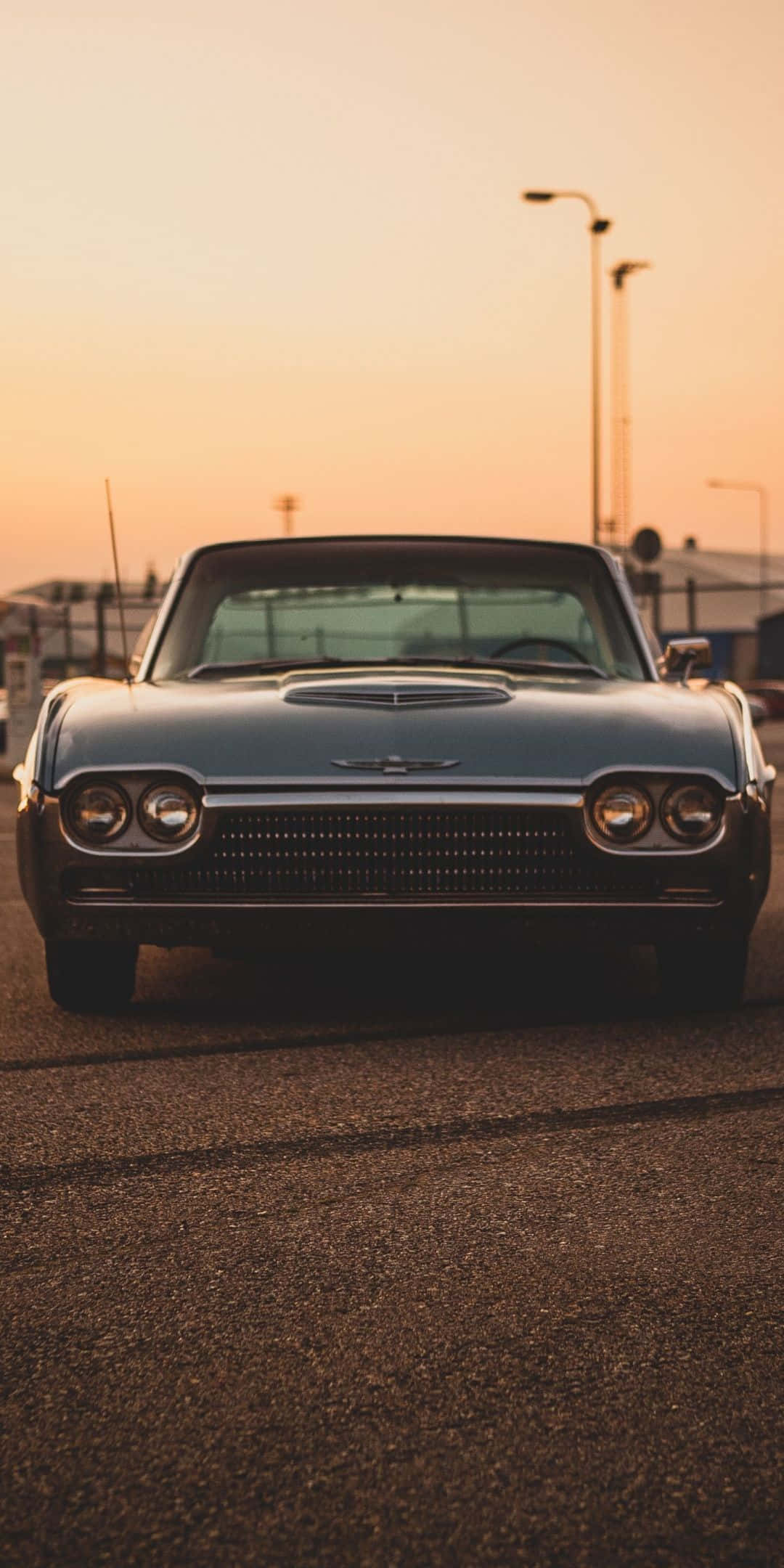 Ford Thunderbird 桌布 壁紙 — 一輛復古藍色敞篷跑車在溫暖的橙色日落天空下，面向前方停在瀝青路上。