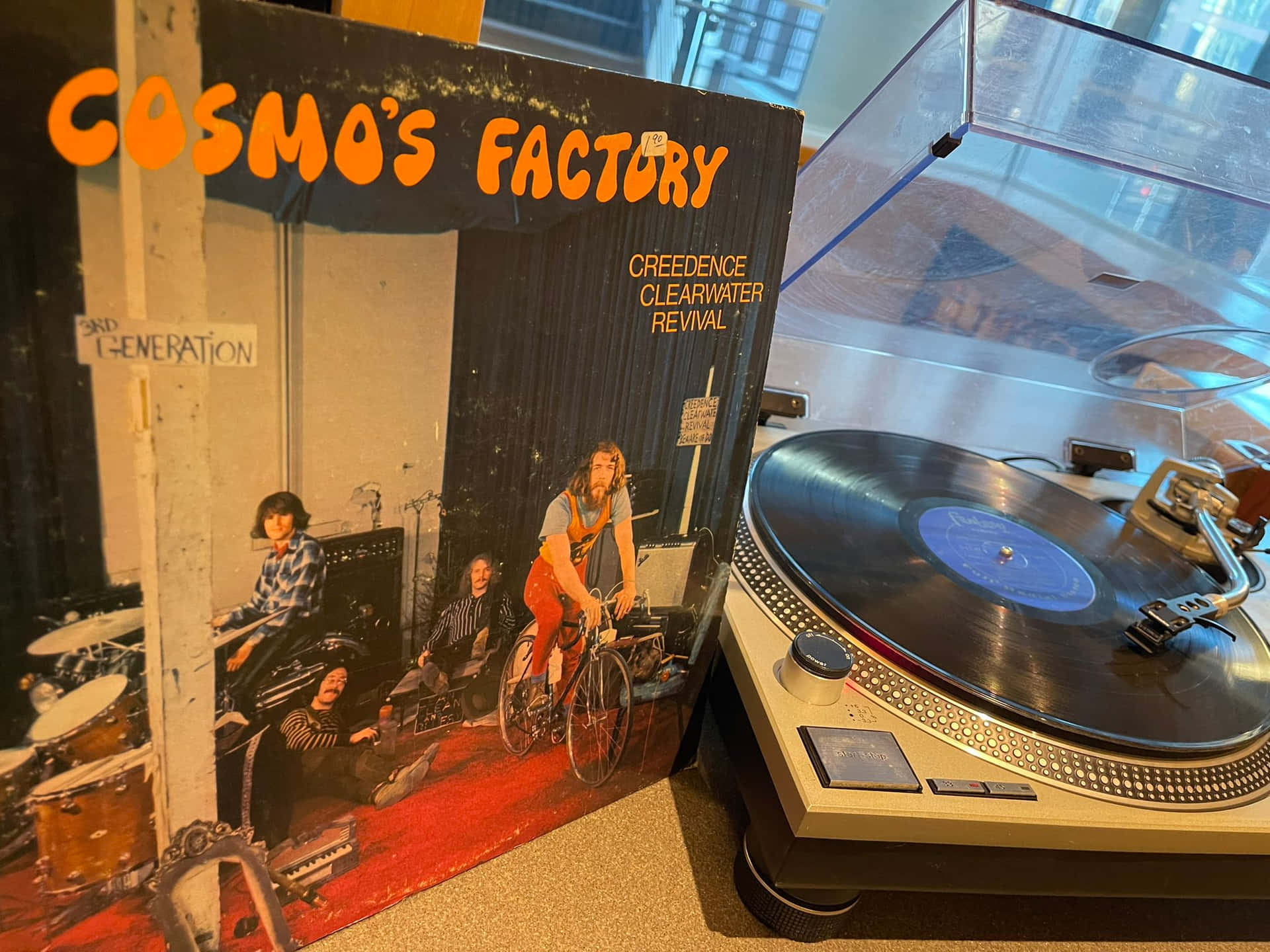  壁紙 — 一張復古的 Creedence Clearwater Revival 專輯封面靠在一個唱盤上，唱盤上的黑膠唱片在玻璃下旋轉。