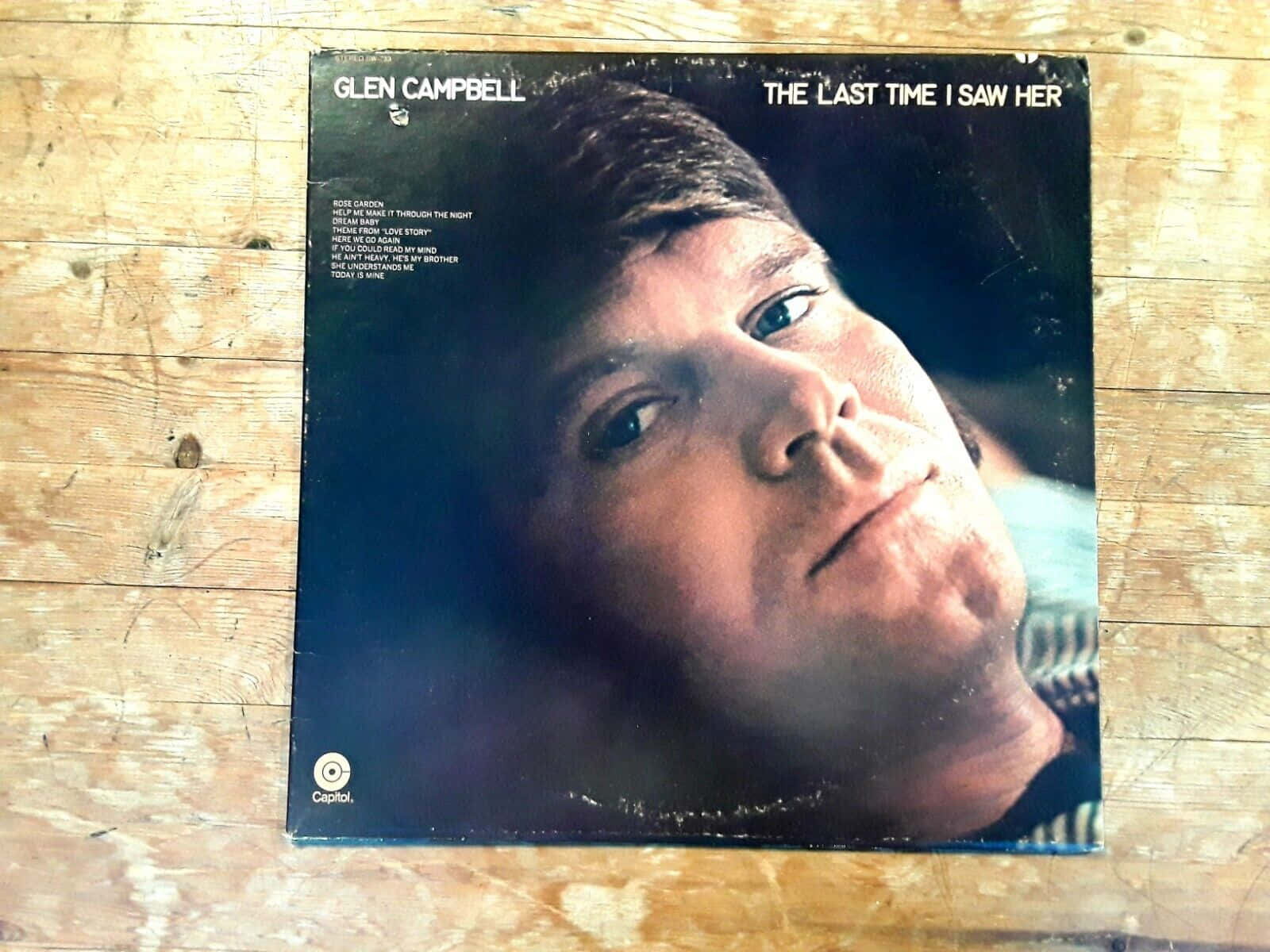  壁紙 — 復古 Glen Campbell 專輯封面放在風化的木板上，溫暖的自然光線照射。