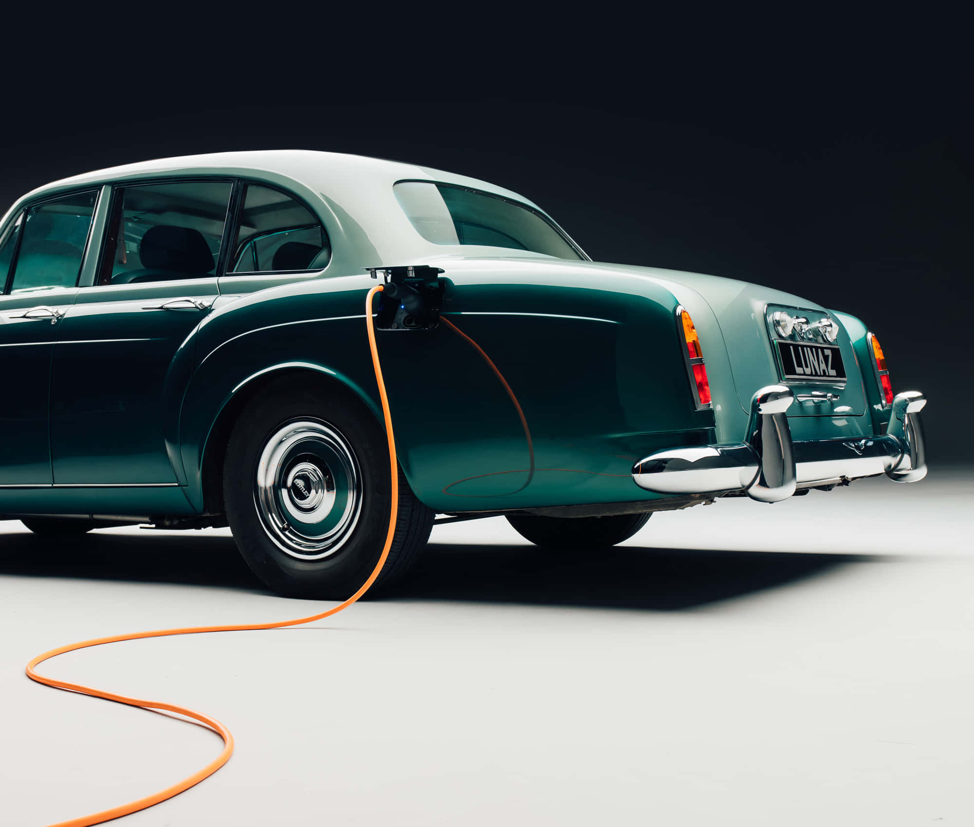Bentley S2 桌布 壁紙 — 一輛帶有鍍鉻裝飾的復古綠色豪華汽車，在黑暗的攝影棚背景下插入一條亮橙色的充電線。