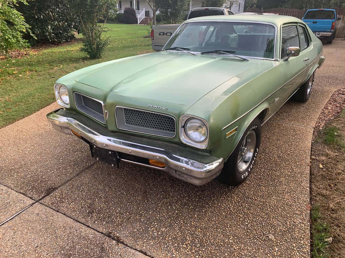 Pontiac Ventura 桌布 壁紙 — 一輛復古橄欖綠色的龐蒂亞克GTO停泊在碎石車道上，背景是郊區房屋和樹木。