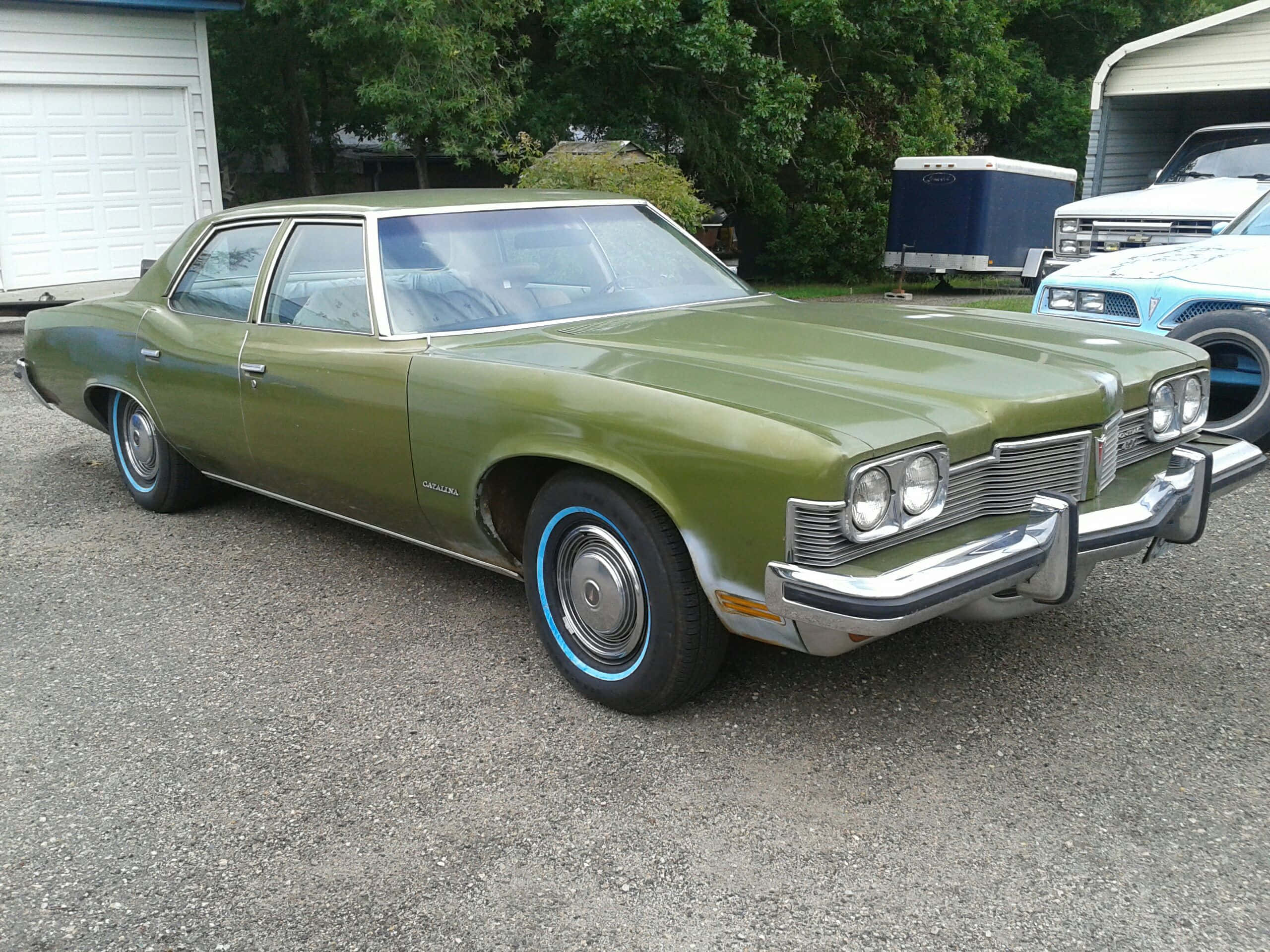 Pontiac Catalina 桌布 壁紙 — 一輛復古橄欖綠色轎車，帶有藍色邊緣的車輪，停在郊區車道的礫石上。