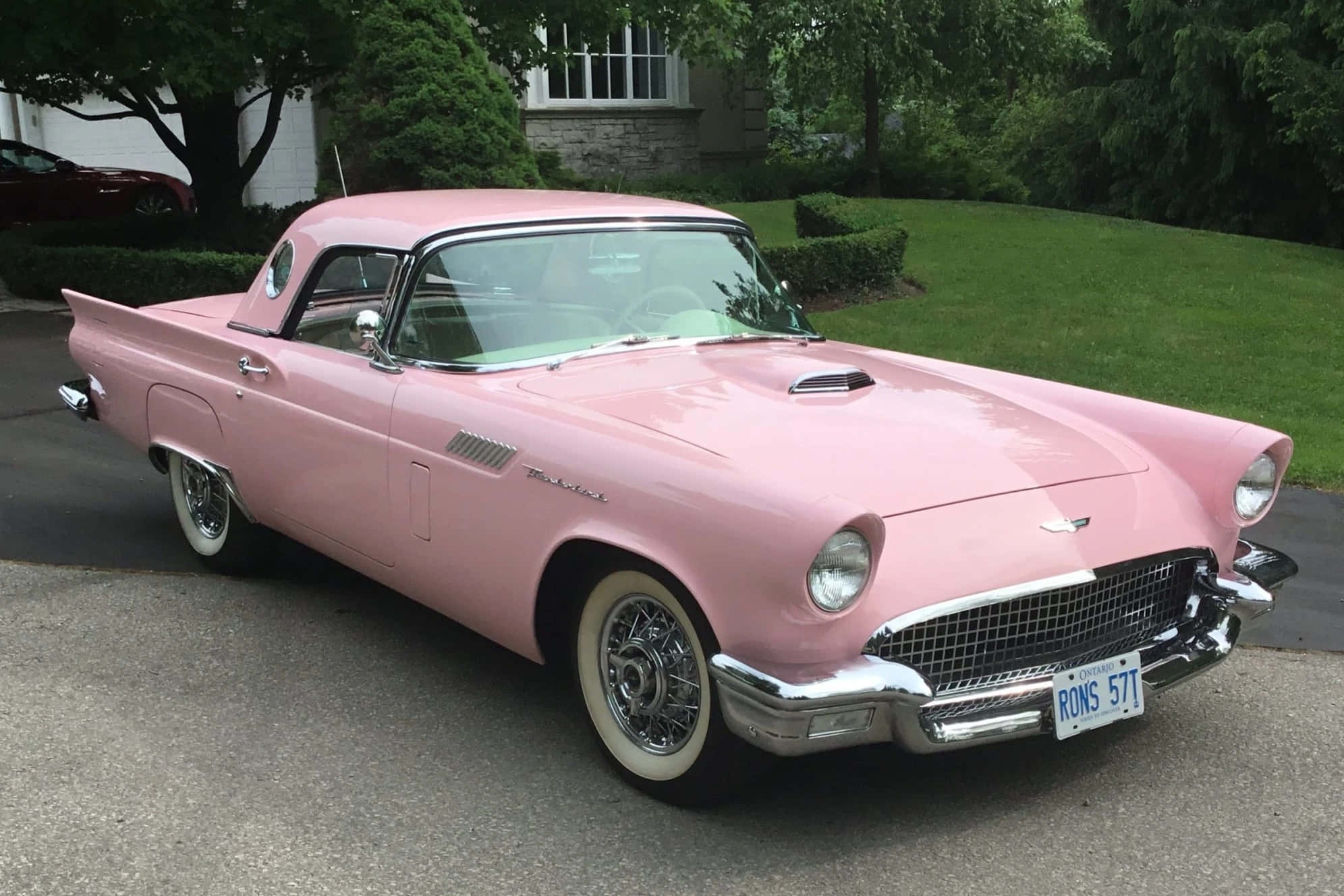 Ford Thunderbird 桌布 壁紙 — 一架復古粉紅色福特雷鳥開篷車停泊在車道上，背景有茂密的綠樹和石屋。