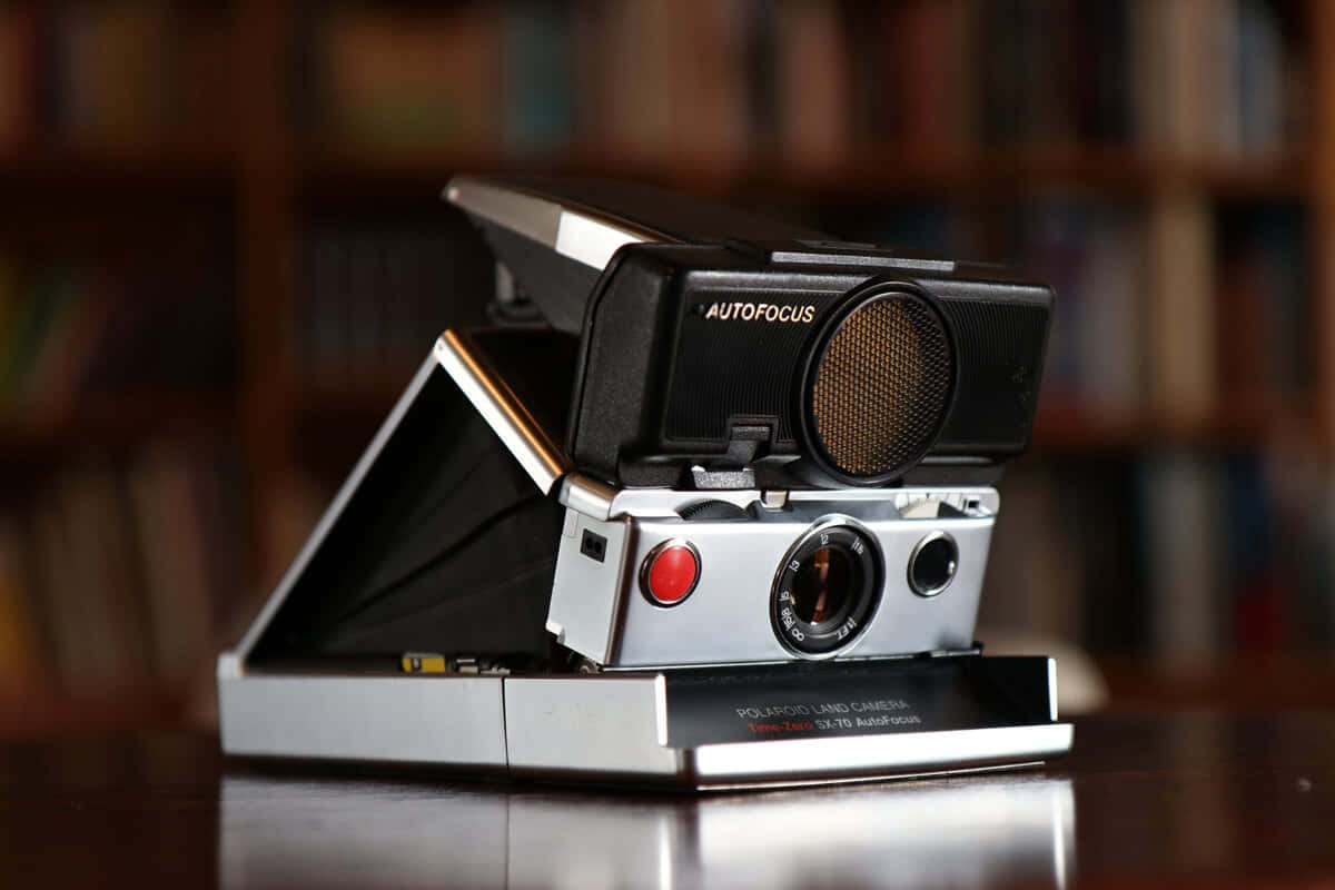  壁紙 — 一部帶有自動對焦功能的復古Polaroid Land Camera打開放在木桌上，背景是模糊的書架。
