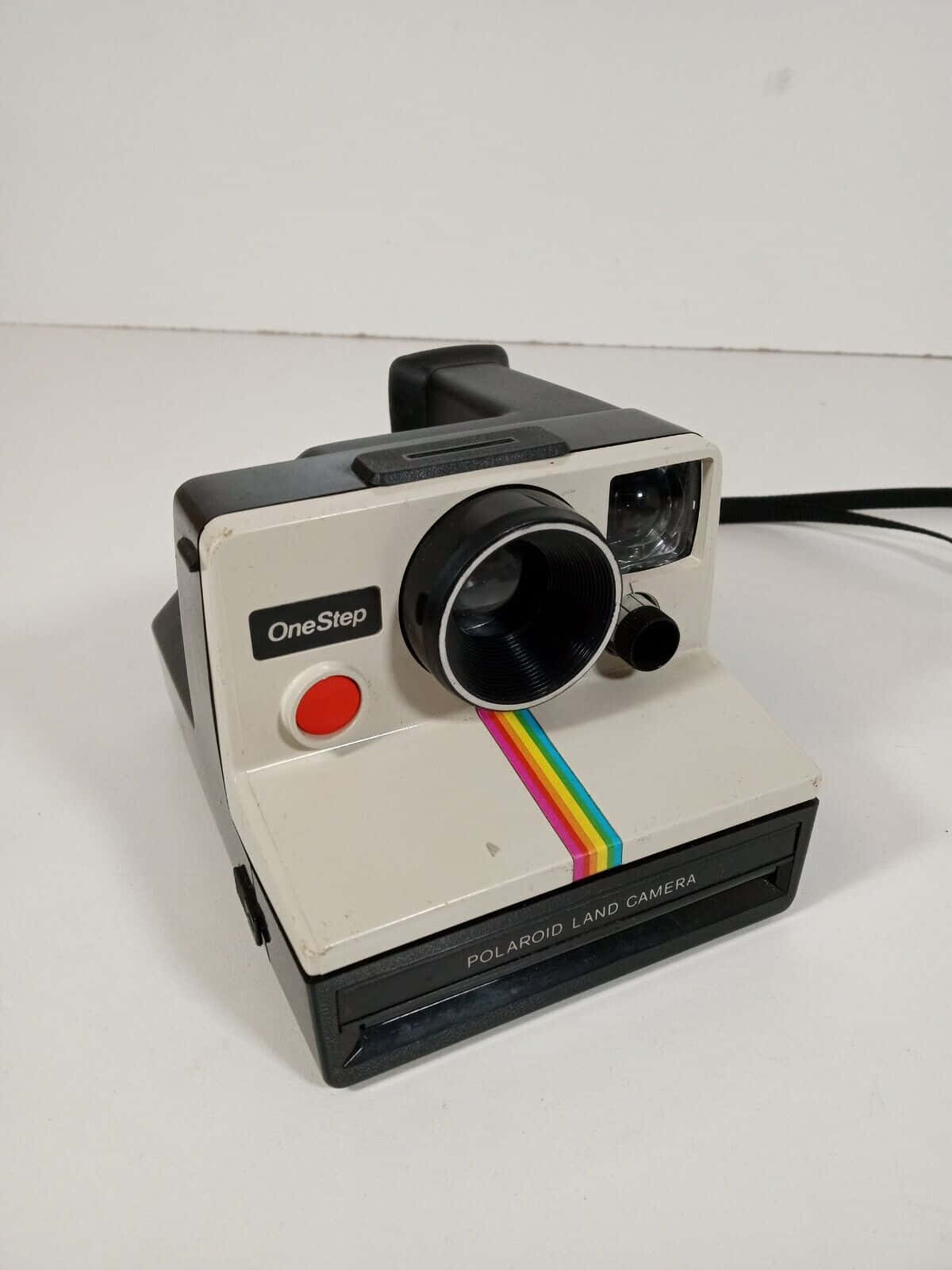  壁紙 — 一部帶有彩虹條紋的復古Polaroid OneStep Land相機放置在純白色表面上。