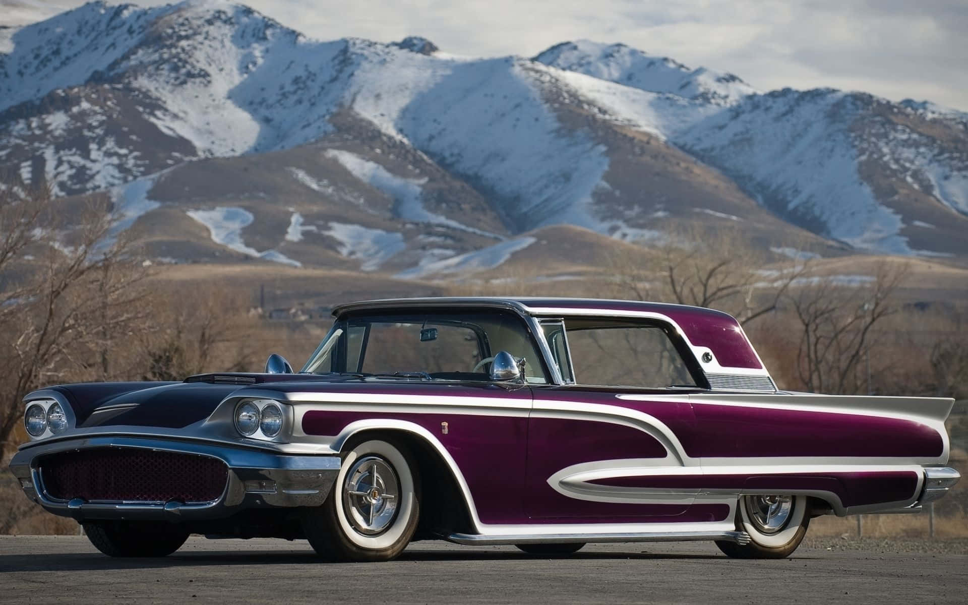 Ford Thunderbird 桌布 壁紙 — 一輛復古紫色和鍍鉻汽車停泊在白雪覆蓋的山脈前，天空多雲。