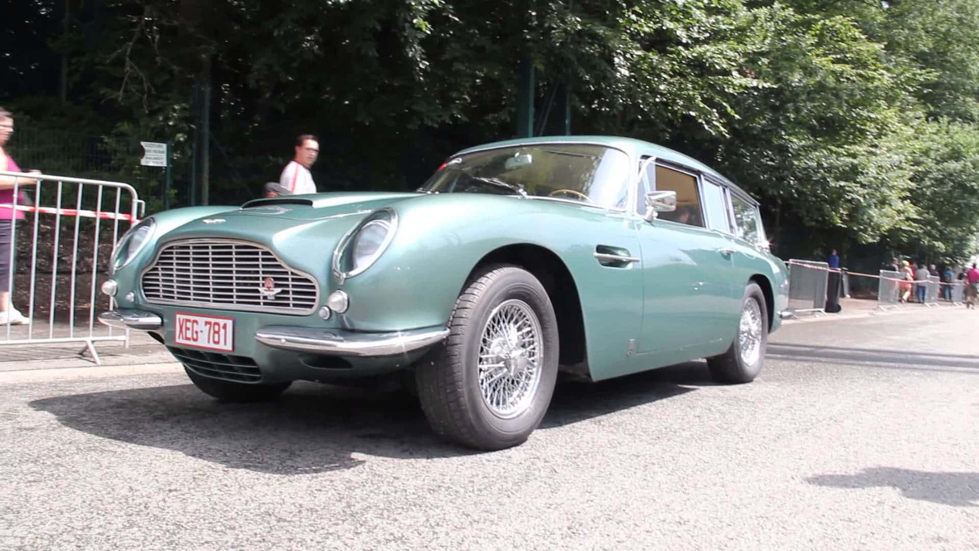 Aston Martin Db5 桌布 壁紙 — 一輛復古青綠色的阿斯頓馬丁DB5旅行車停在碎石路上，背景有樹木和觀眾。
