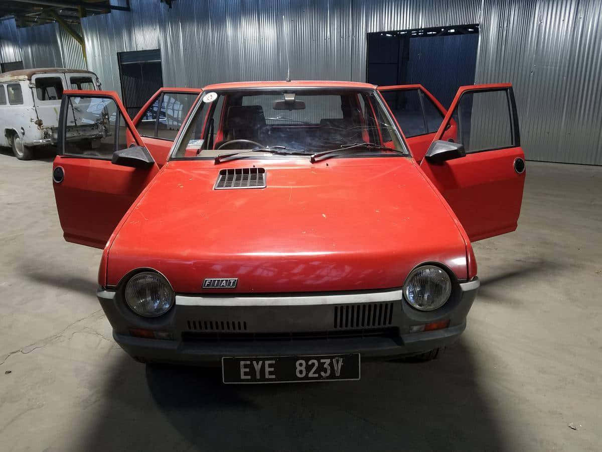 Fiat Ritmo 桌布 壁紙 — 一輛復古紅色Fiat 126，所有車門打開，停在金屬牆車庫內，在明亮的人造光下。