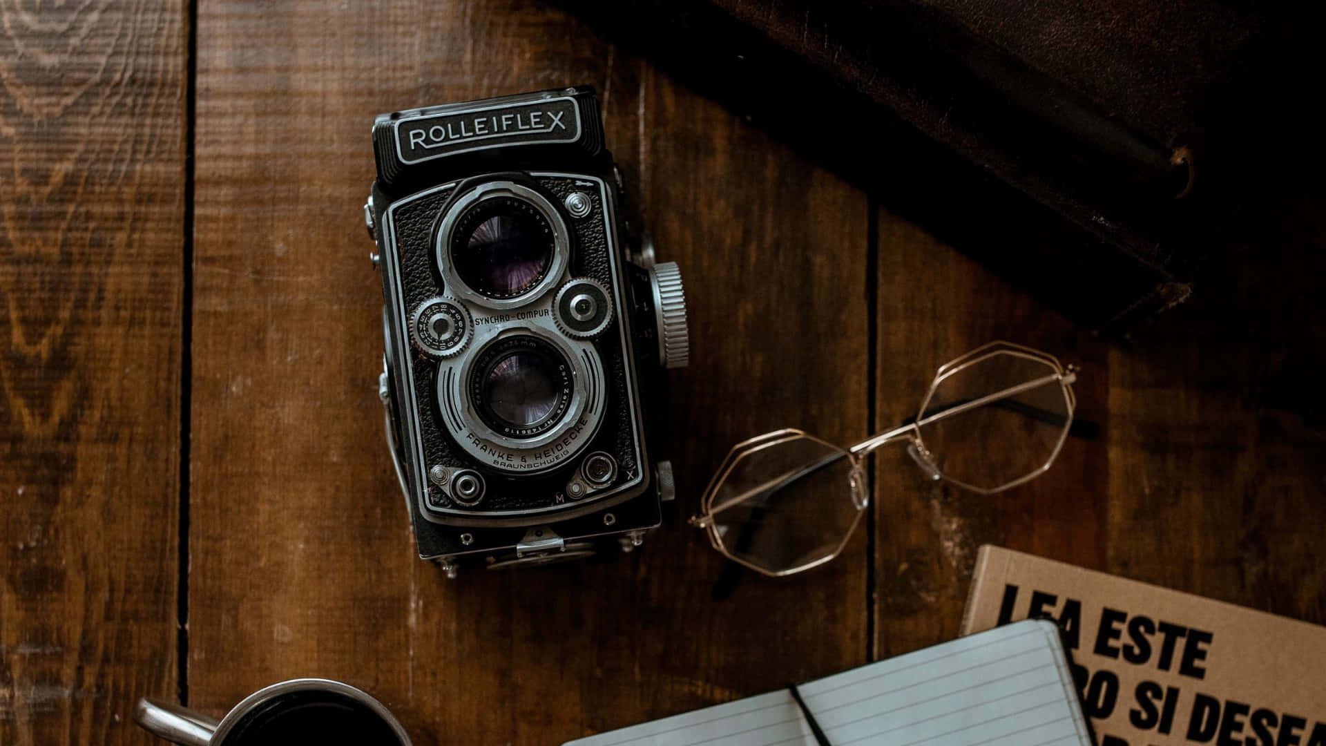  壁紙 — 經典 Rolleiflex 相機放置在質樸的木桌上，旁邊有眼鏡、筆記本和咖啡杯。