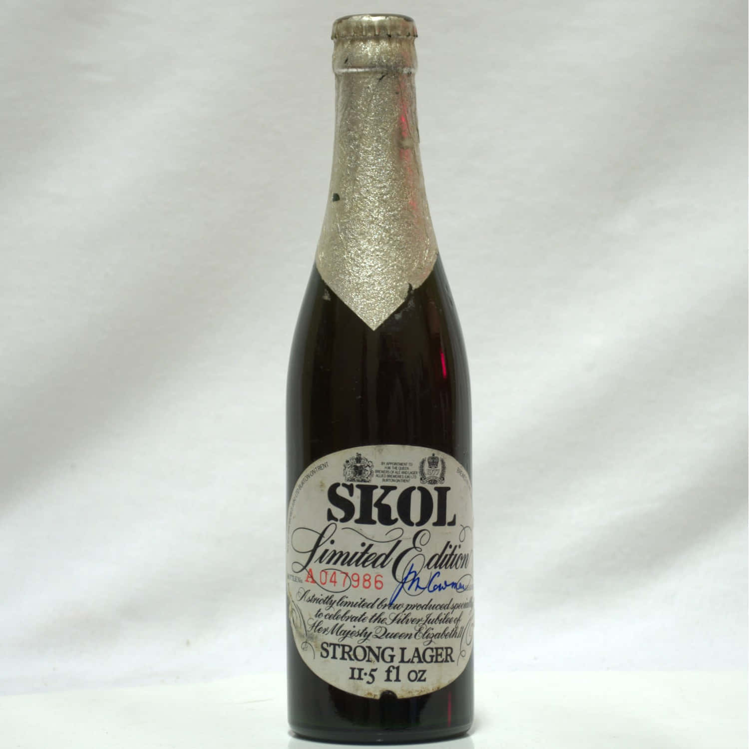 壁紙 — 一個復古的Skol Strong Lager啤酒瓶，帶有銀箔頸部和手寫簽名標籤，背景為純白色。