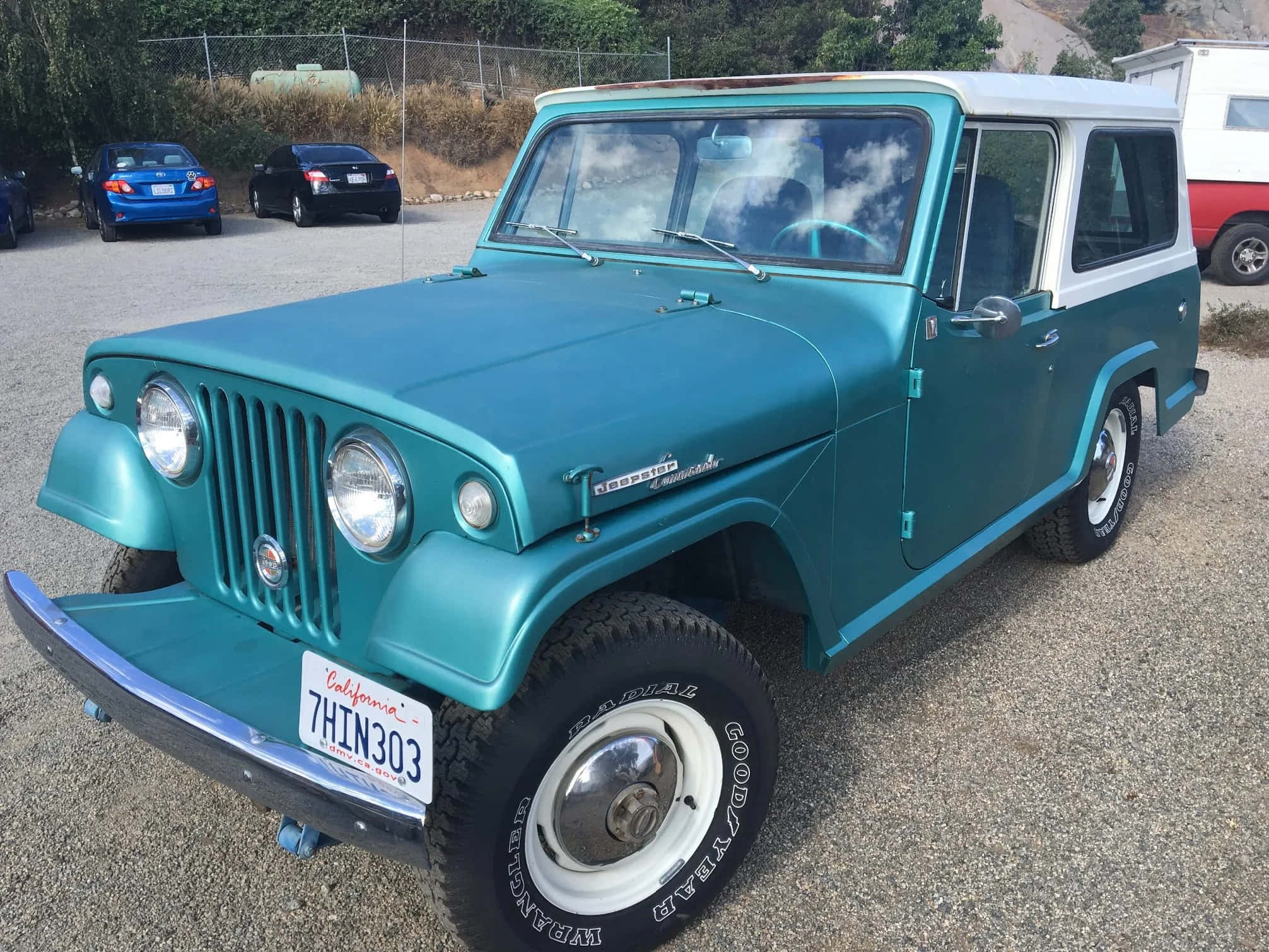 Jeepster 桌布 壁紙 — 一輛復古青綠色和白色的Jeepster Commander停泊在碎石上，背景有其他車輛。