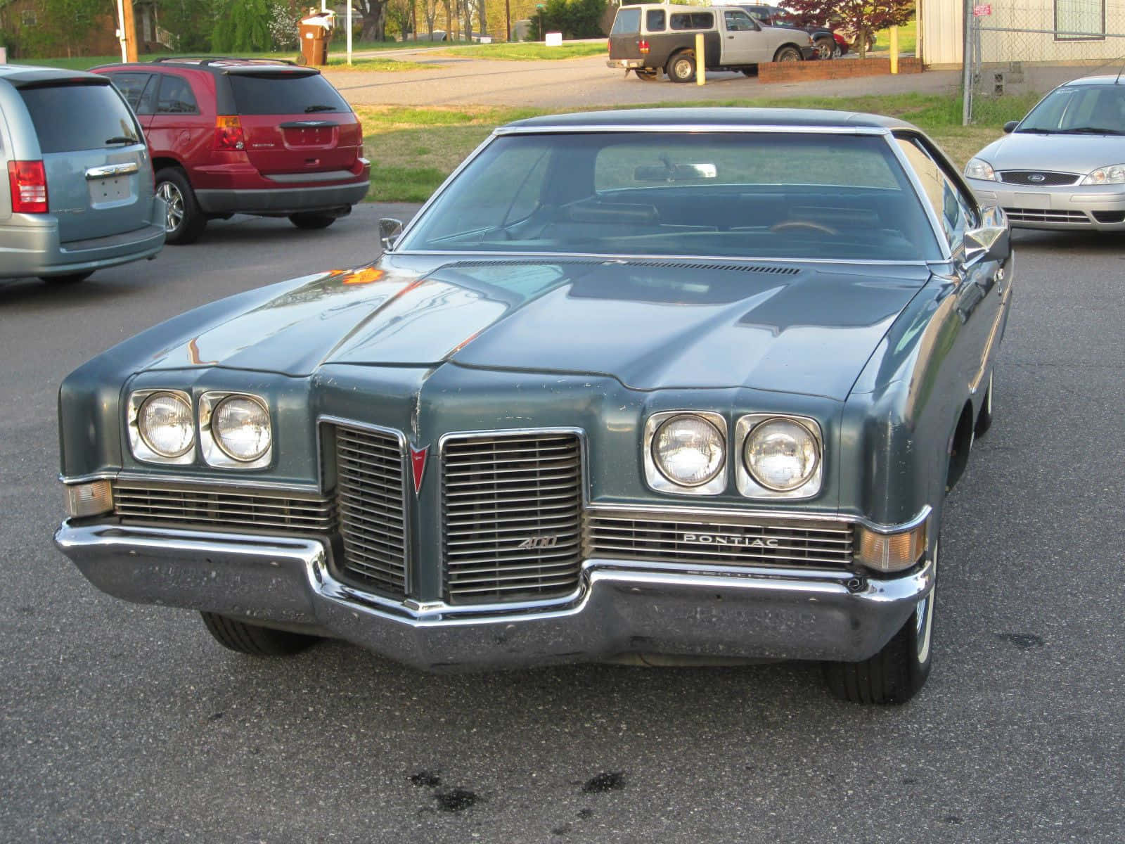Pontiac Catalina 桌布 壁紙 — 一輛復古青綠色的龐蒂亞克格蘭普里茲在日光下閃耀，停放在一個郊區停車場，周圍有其他汽車。