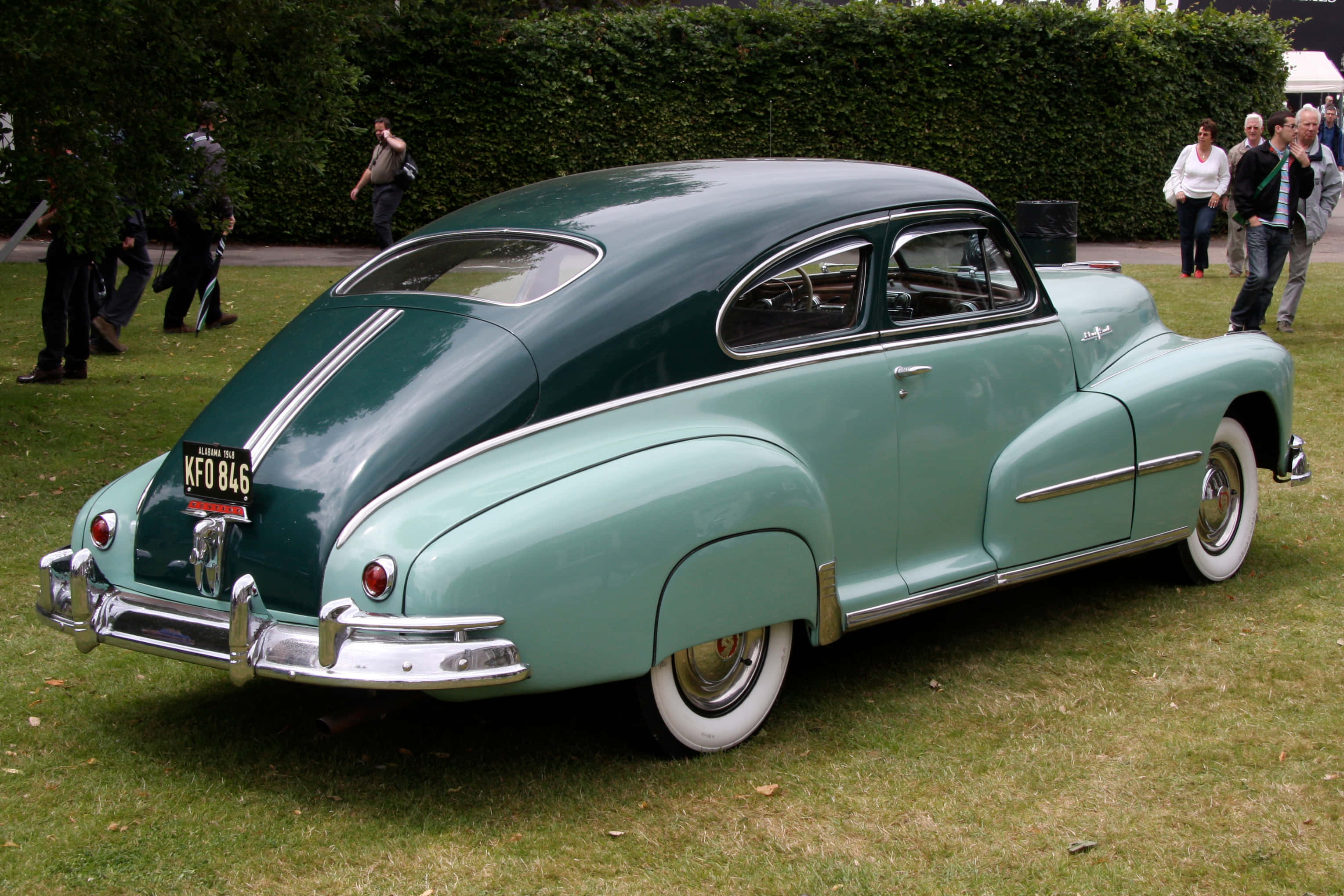 Pontiac Streamliner 桌布 壁紙 — 一輛復古雙色調綠色和藍綠色的經典汽車，帶有鍍鉻裝飾，停在草地上，附近有人。