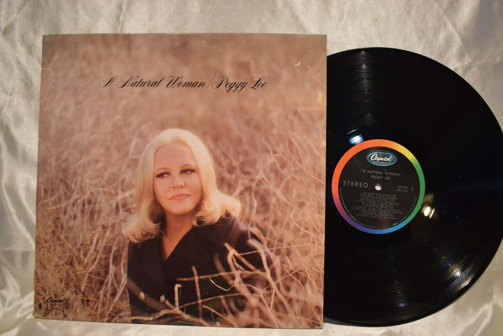  壁紙 — Peggy Lee 的《A Natural Woman》復古黑膠唱片和專輯封面放在白色布料表面上。