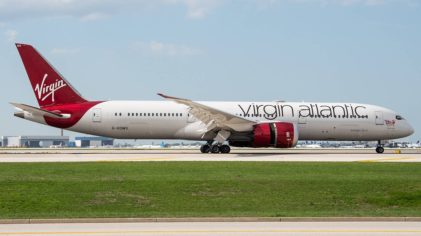 Virgin Atlantic航空飛機準備登機 壁紙 — 一架維珍航空波音787夢想客機在陽光明媚的機場跑道上滑行，背景有綠草和機庫。