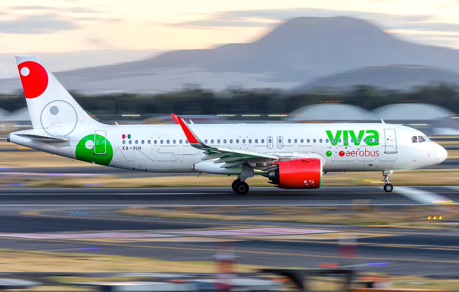 Viva Aerobus 機場模糊效果拍攝 壁紙 — 一架Viva Aerobus飛機在黃昏時分在跑道上加速，帶有模糊的動態和遠處山脈在柔和粉彩光中。