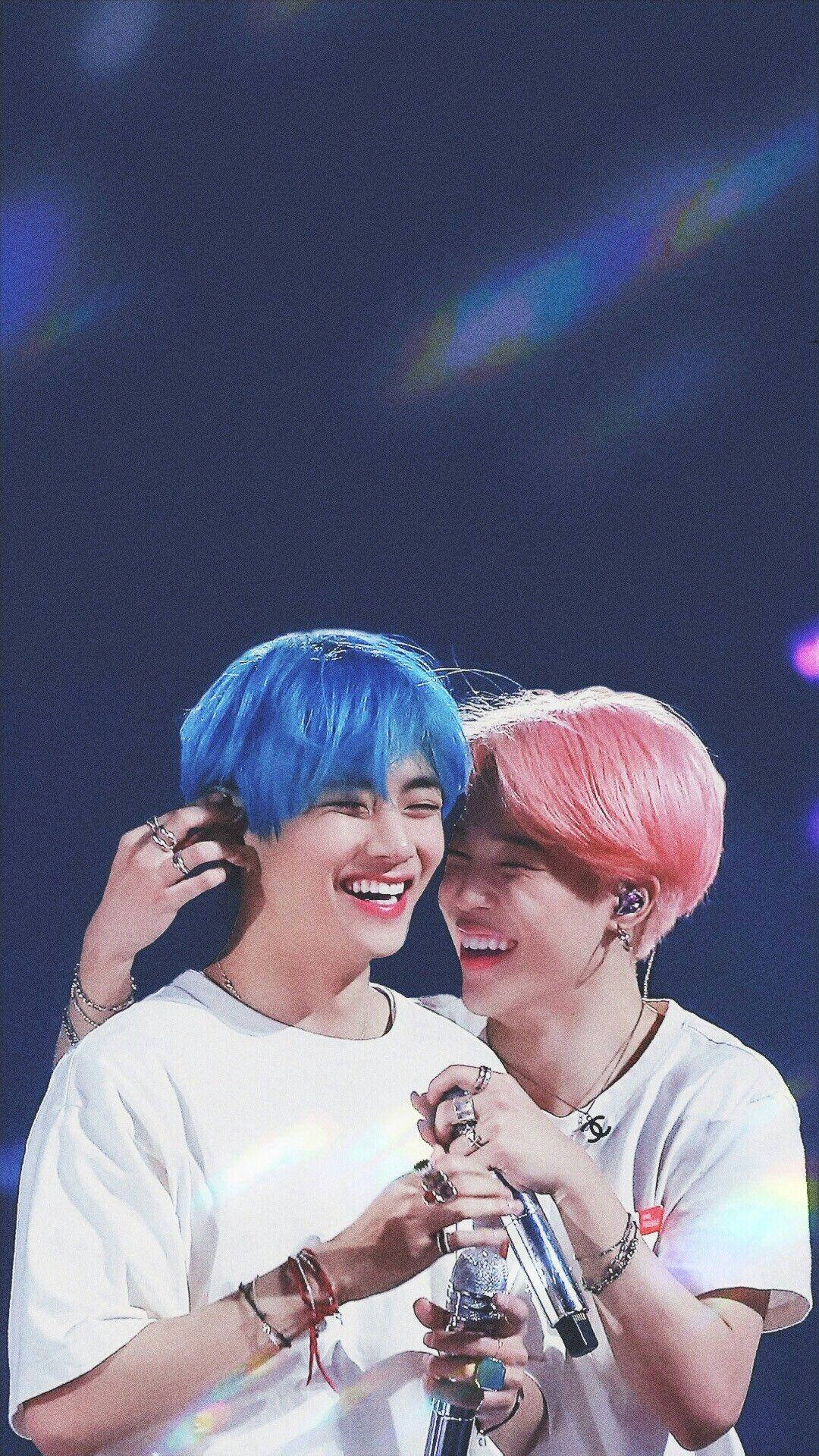 Vmin BTS 演唱會瞬間 壁紙 — 兩位笑容滿面的表演者，一頭藍色和粉紅色頭髮，在色彩繽紛的燈光下於充滿活力的舞台上分享歡樂時刻。