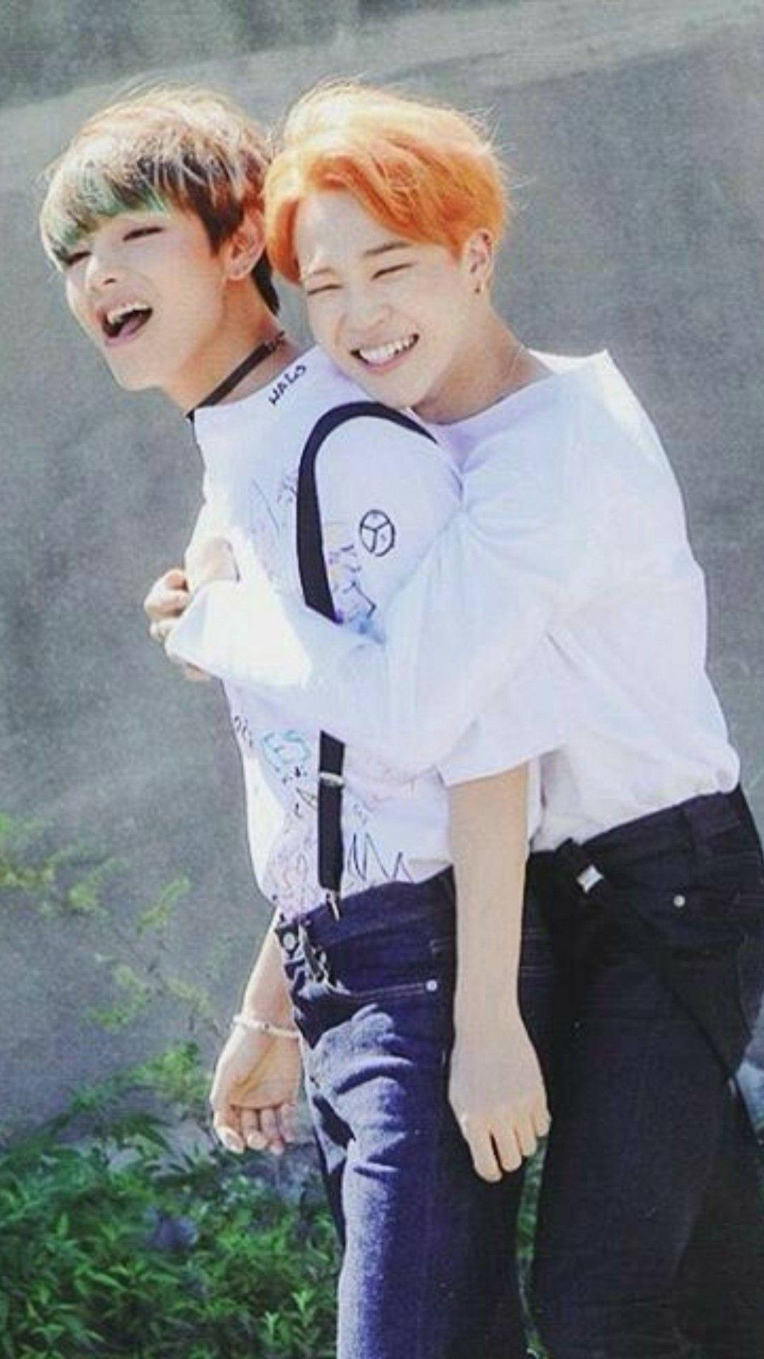 Vmin 背擁瞬間 壁紙 — 兩位頭髮色彩繽紛的年輕男子，一人抱著另一人，在戶外嬉戲擁抱，開懷大笑。