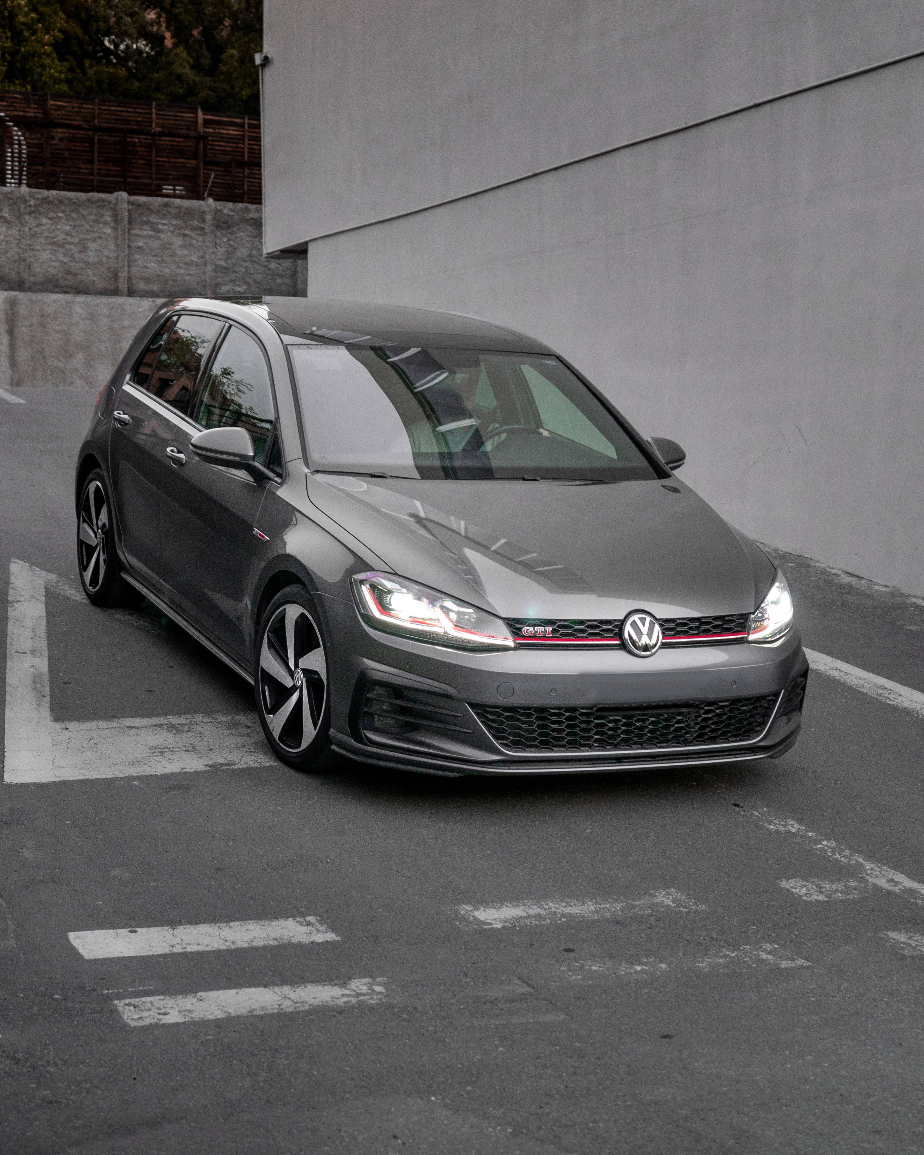 Volkswagen Golf GTI MK7.5 黑色 壁紙 — 一架時尚的灰色福士 Golf GTI 停泊在混凝土停車場，地上有白色標線，背景為簡約的城市景觀。