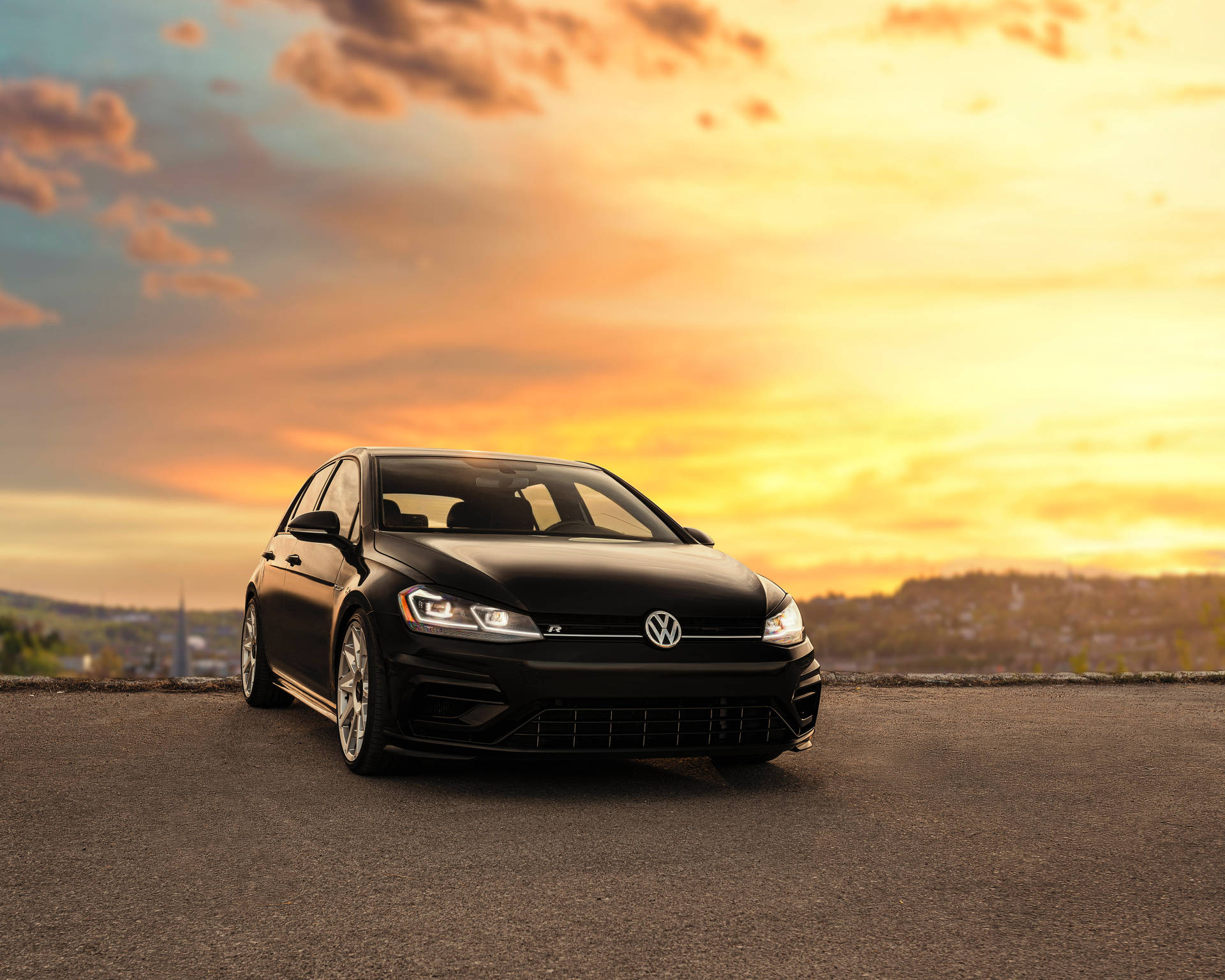 黑色Volkswagen Golf R在日落時停在道路上，天空橙色，有山丘。