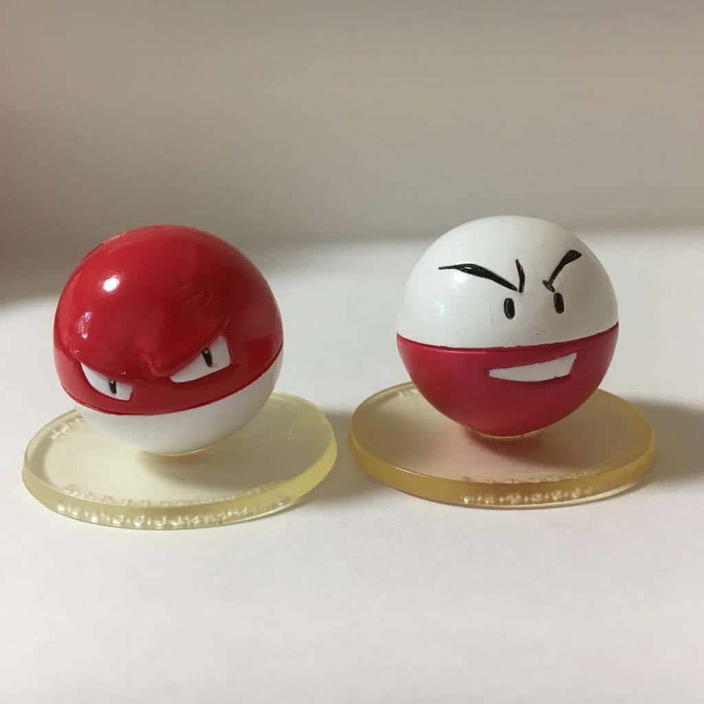 Voltorb - 寶可夢系列中的電系寶可夢 壁紙 — 兩個憤怒嘅寵物小精靈主題波波，帶有兇猛嘅表情，並排企喺透明支架上，背景係純色。