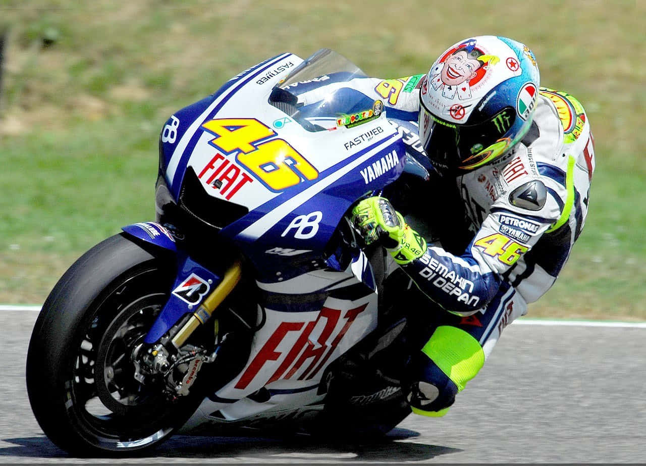 VR46 2009捷克大獎賽 壁紙 — 一名電單車車手在陽光明媚的賽道上急劇傾斜入彎，戴著色彩繽紛的頭盔和賽車服。