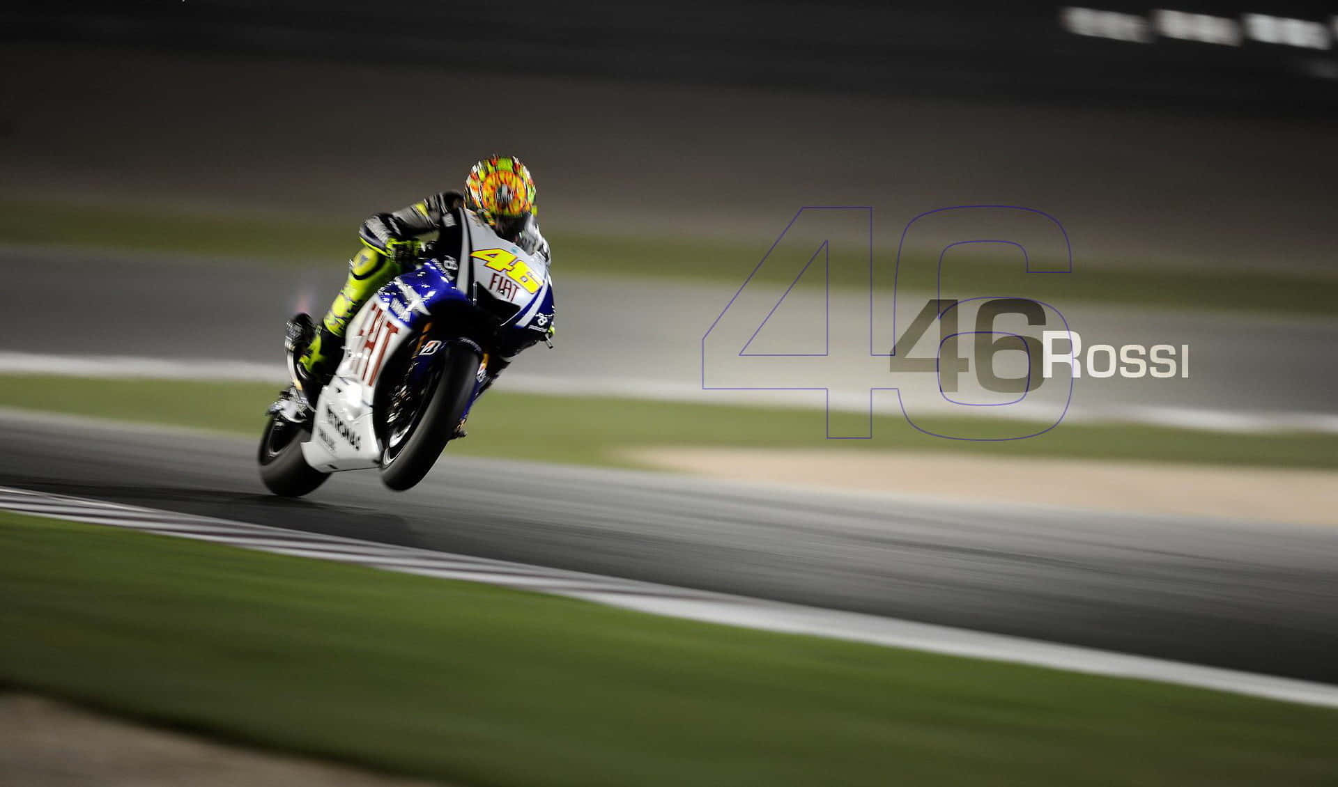 VR46 專業賽車編號 壁紙 — 電單車手在人造燈光下的賽道上傾斜入彎，帶有 '46 Rossi' 水印。