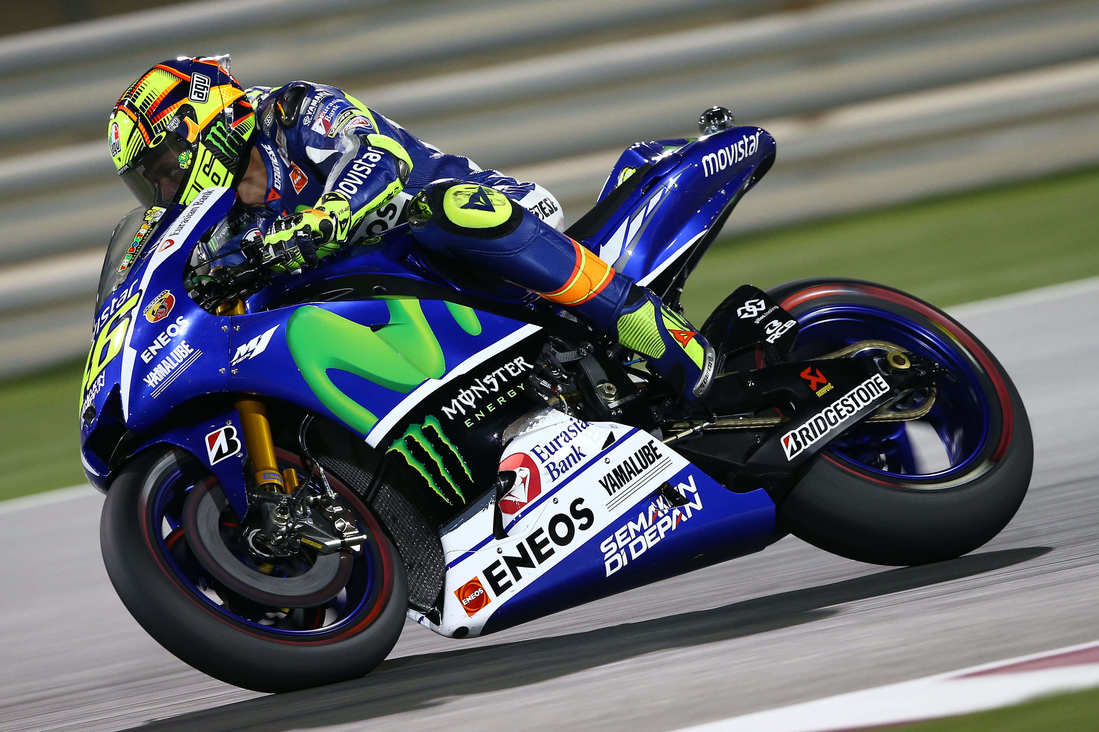 VR46 職業大獎賽賽車手 壁紙 — 一名電單車賽車手在高速賽道活動中，騎著藍綠色的賽車傾斜入彎。