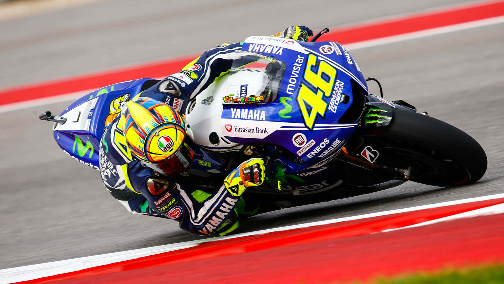 VR46 低姿彎道騎乘 壁紙 — 一位電單車賽車手在賽道上穿著鮮豔的藍黃色賽車服，號碼46，急劇傾斜入彎。
