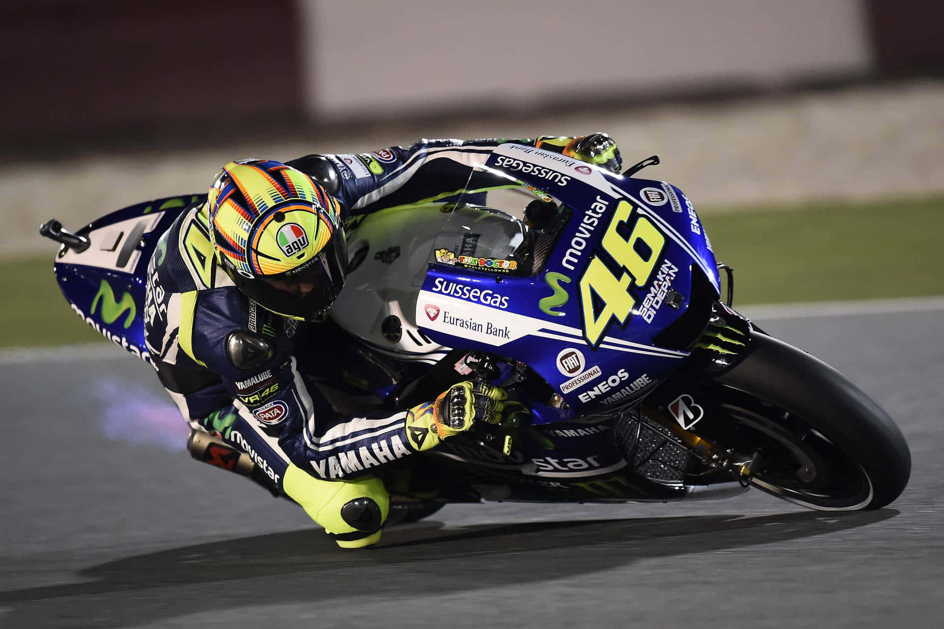 VR46 在美國大獎賽中的競速風采 壁紙 — 一位電單車車手在夜間賽道上急彎傾斜，戴著鮮豔的頭盔和藍色Yamaha賽車服。