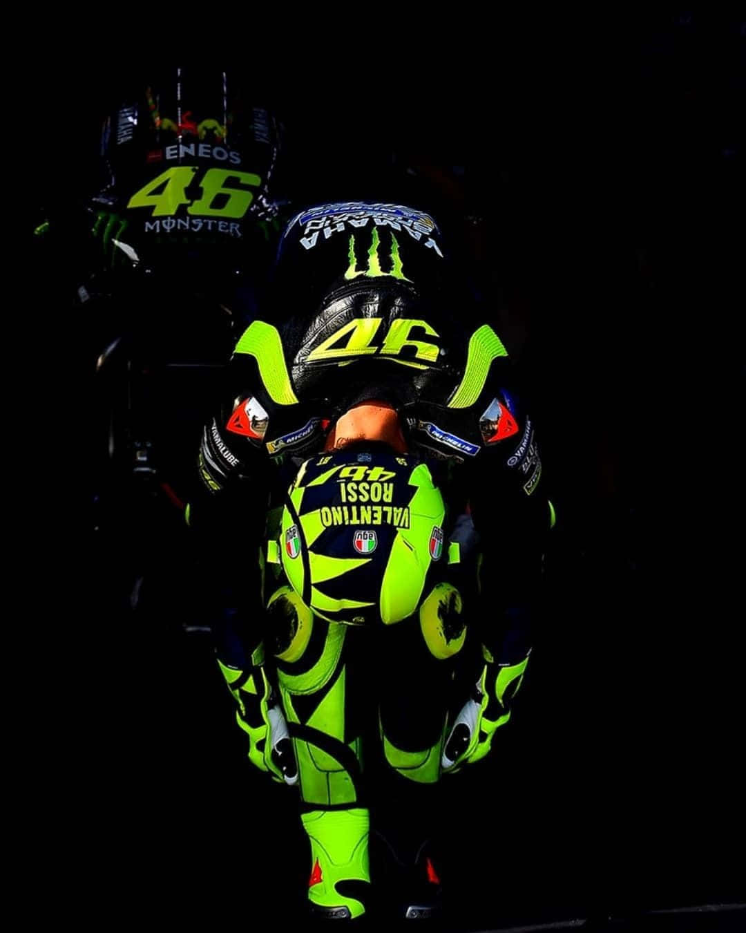 VR46 意大利賽車明星 Valentino Rossi 壁紙 — 一名電單車手身穿螢光綠和黑色賽車裝備，背上印有46號和「Valentino Rossi」，在黑暗背景前低伏著。