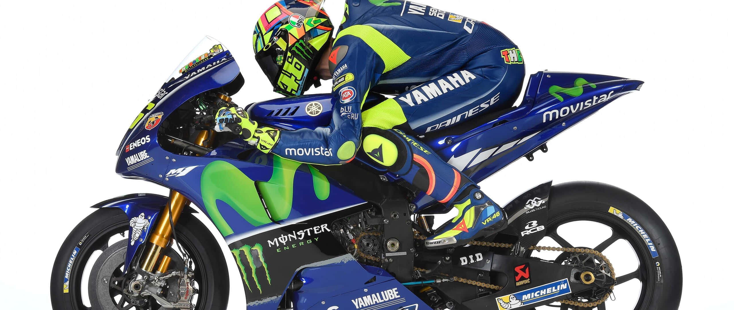 VR46 雅馬哈 Monster Energy 賽車的極速體驗 壁紙 — 一位身穿藍色和螢光綠色裝備的Yamaha MotoGP車手，在純白色背景前，騎著品牌賽車傾斜入彎。