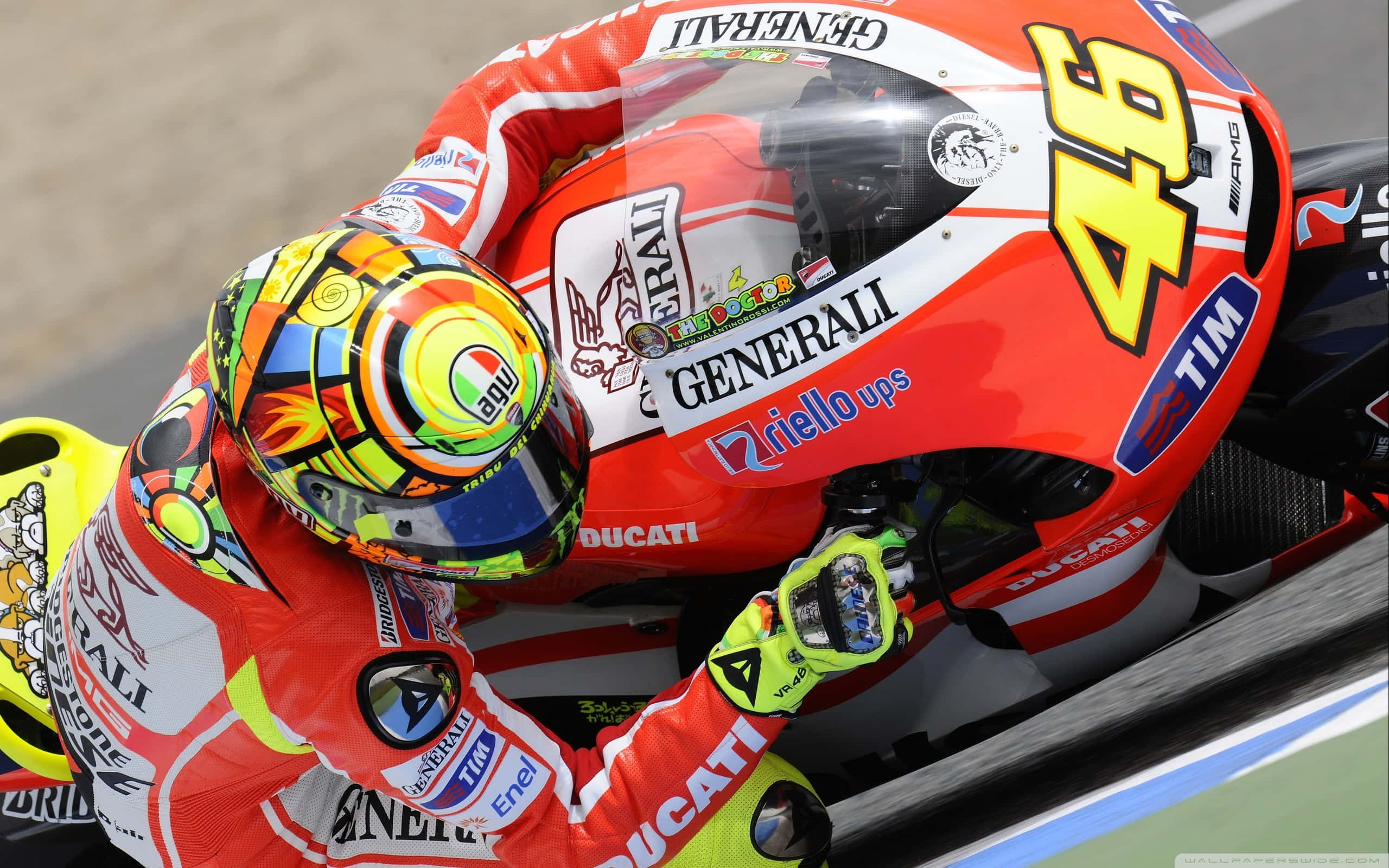 VR46 駕駛紅色杜卡迪賽車 壁紙 — 一名身穿鮮紅色裝備的電單車手，戴著色彩繽紛的頭盔，駕駛 Ducati 電單車在賽道上急劇傾斜入彎。