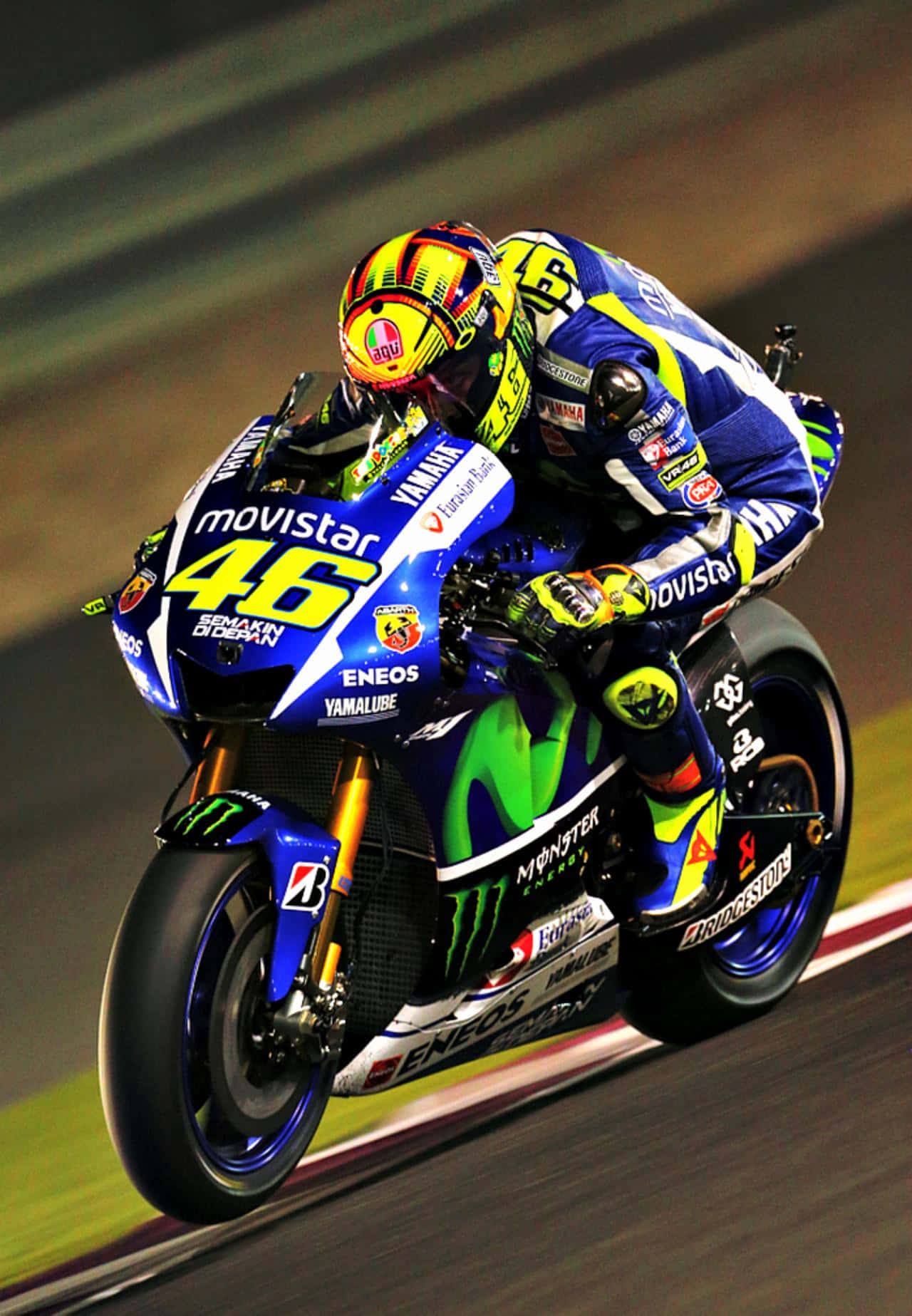 VR46職業大獎賽冠軍 壁紙 — 一位電單車賽車手在夜間燈光明亮的賽道上傾斜入彎，身穿鮮豔的藍綠色賽車服，帶有贊助商標誌。