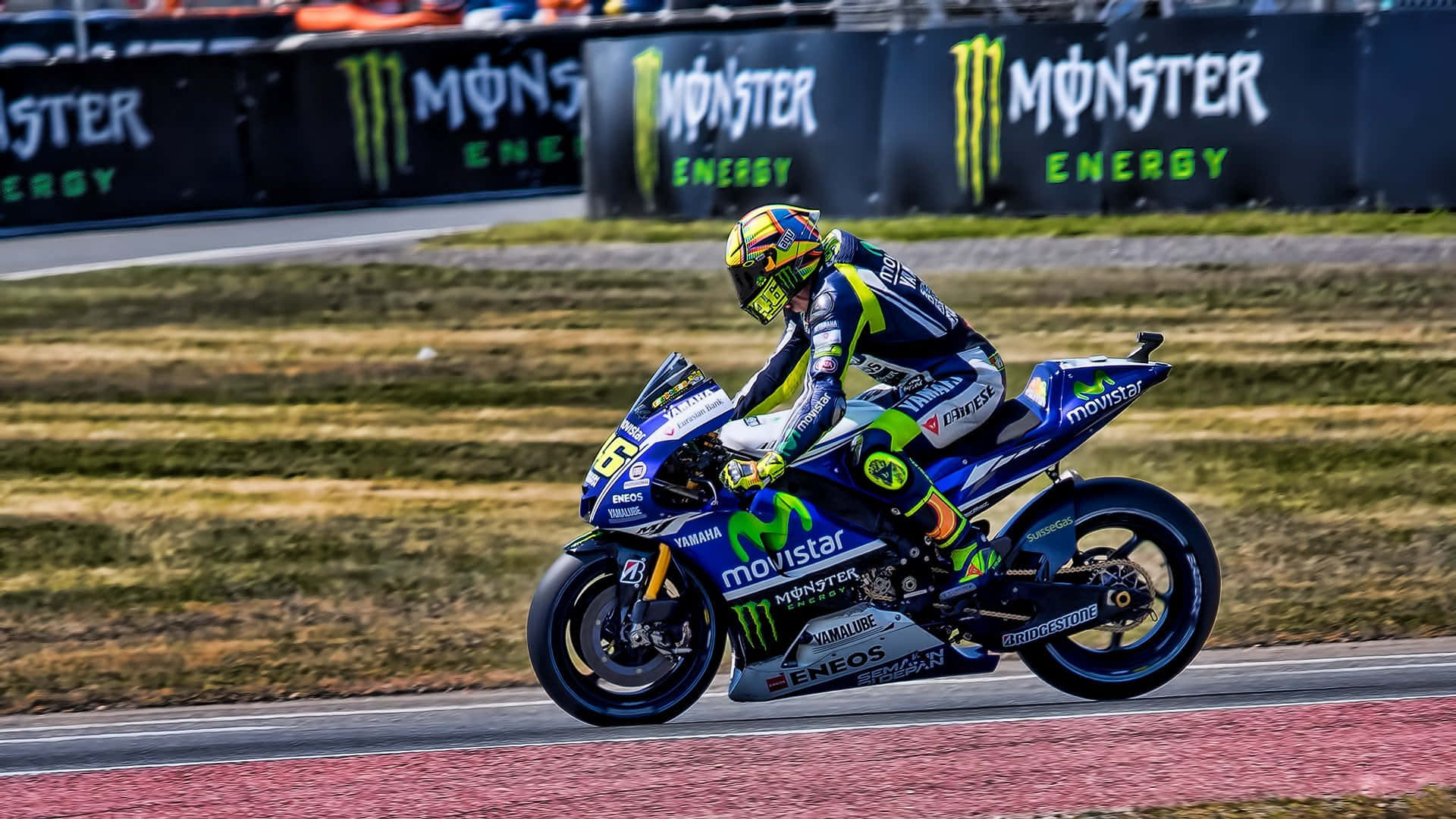 VR46雅馬哈MotoGP賽車隊 壁紙 — 一位電單車車手在賽道上騎著藍色Yamaha電單車，車身飾有Monster Energy標誌，傾身入彎。