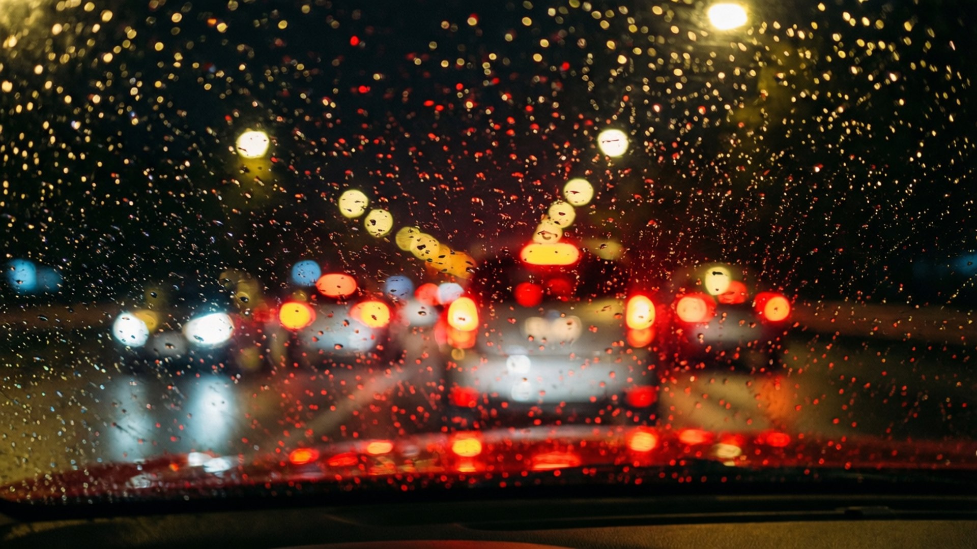 夜間汽車擋風玻璃上的雨滴與模糊的城市燈光