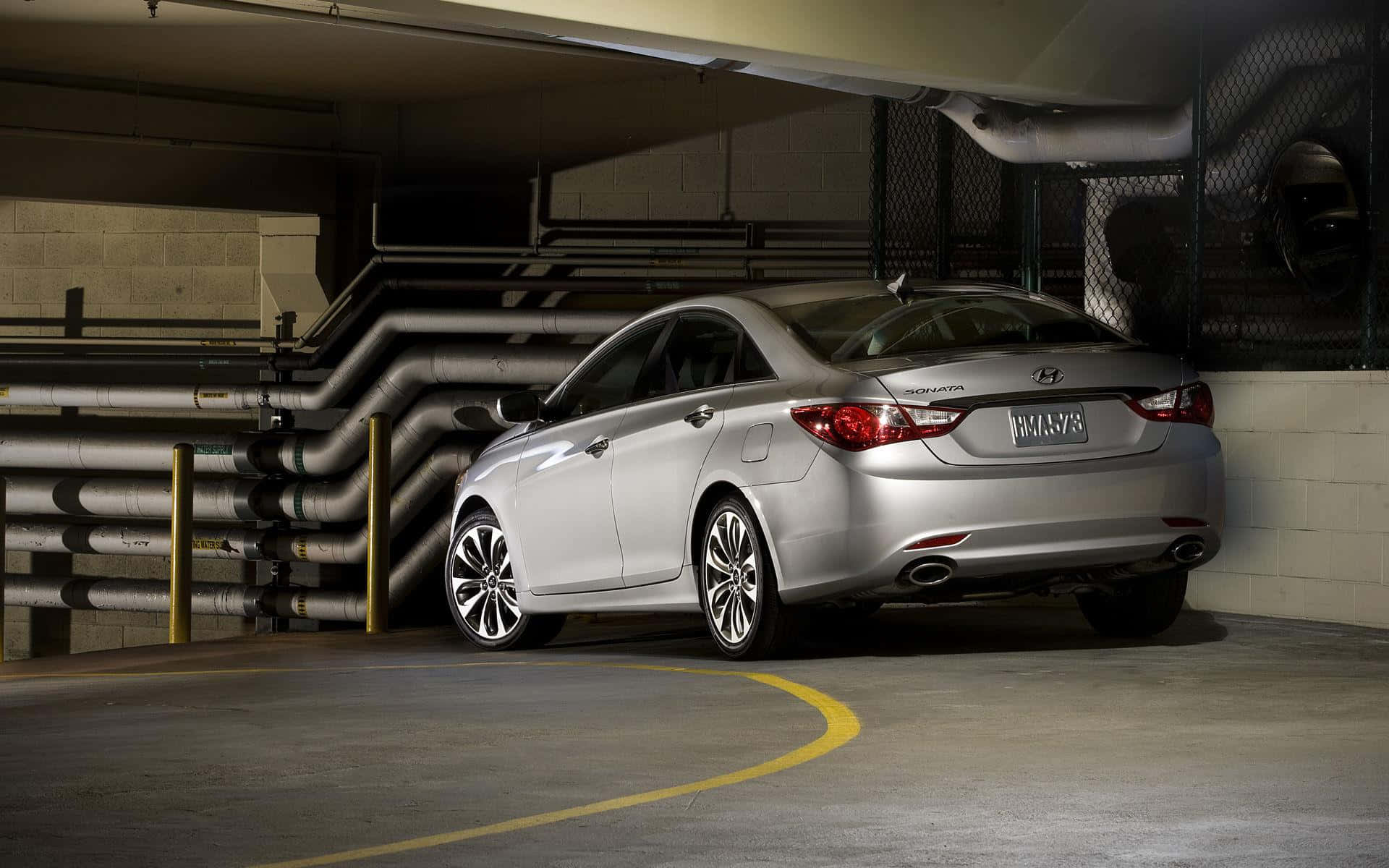 Hyundai Sonata 桌布 壁紙 — 一架時尚的銀色轎車停泊在光線昏暗的地下停車場，內有工業管道和黃色標線。