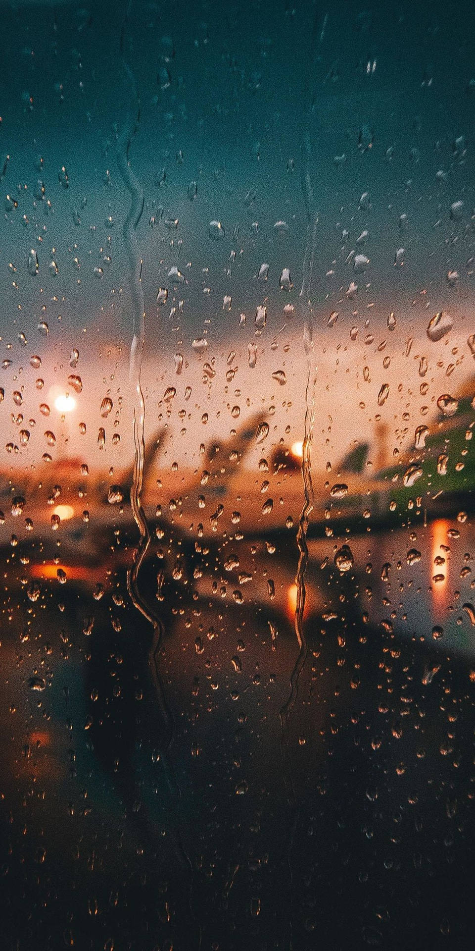 暮色中窗戶上的雨滴與模糊的城市燈光