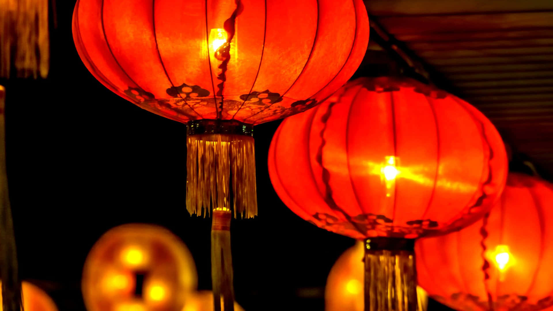  壁紙 — 溫暖發光的紅色紙燈籠帶有流蘇，懸掛在深色背景上，投射出柔和的光線。