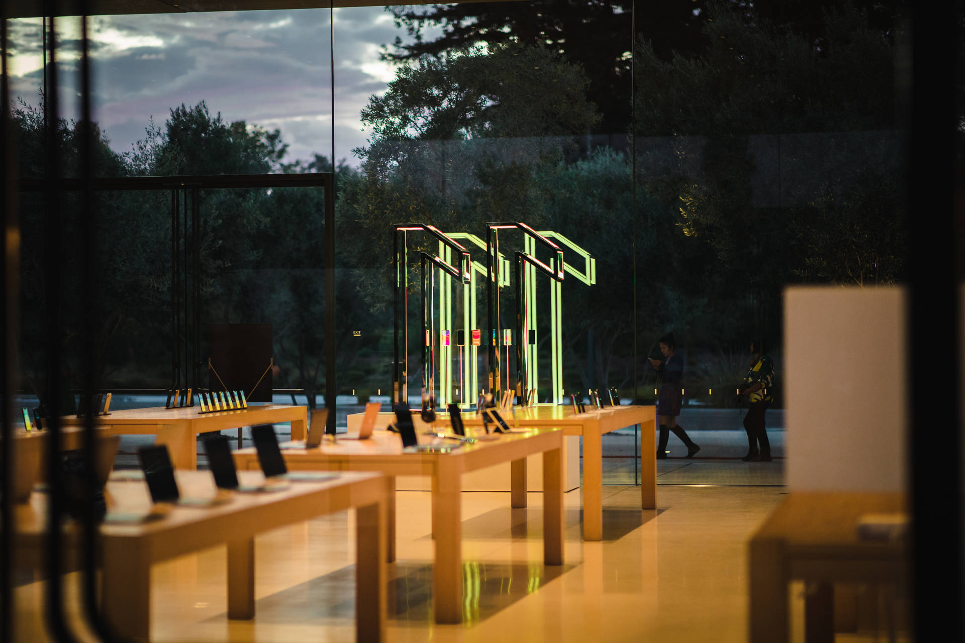 Apple Store內部，發光的產品展示和黃昏時分在外面行走的人們。