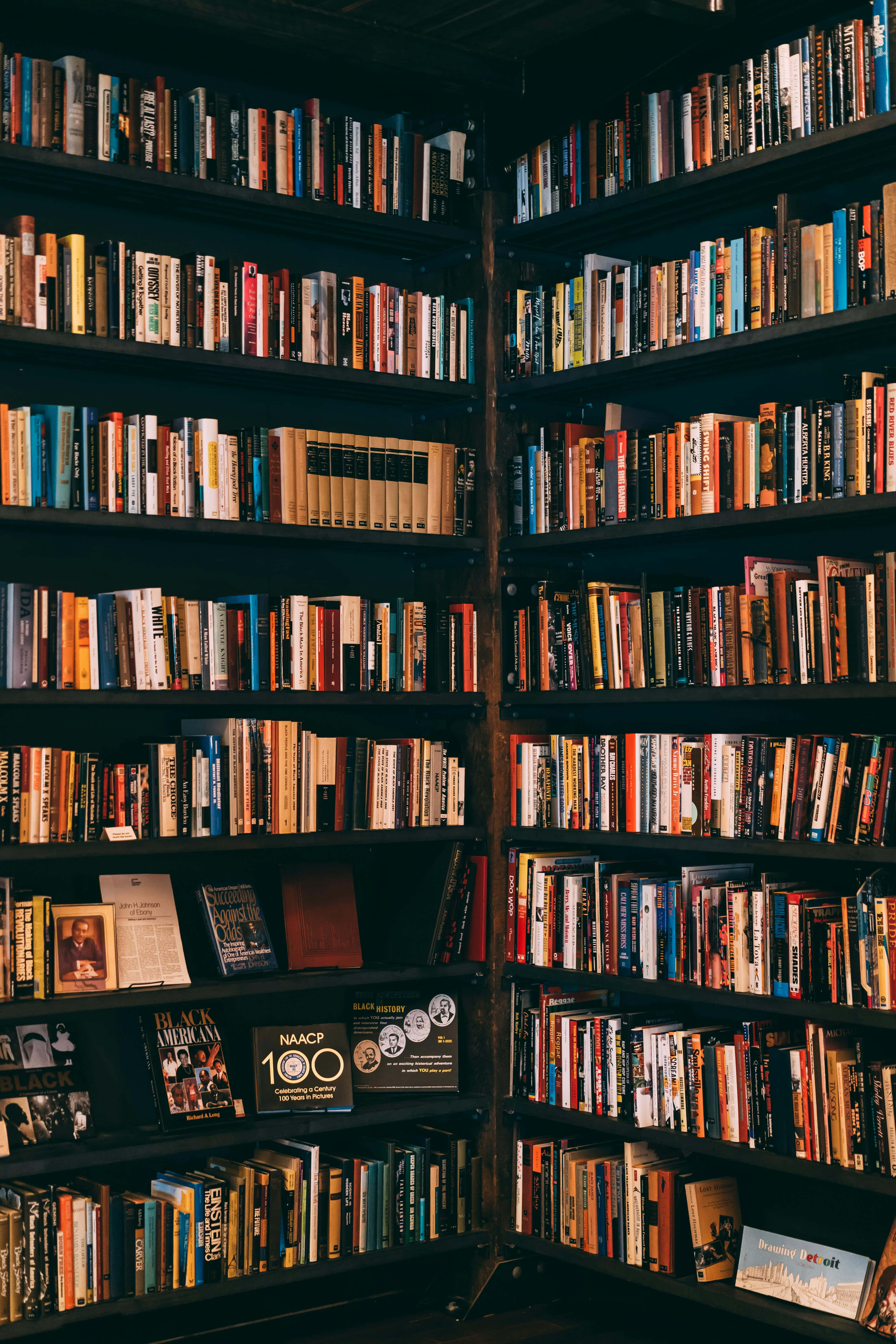 Dark Book Aesthetic 桌布 壁紙 — 溫暖照明的舒適圖書館角落，高書架上擺滿色彩繽紛的書籍，營造出學術氛圍。
