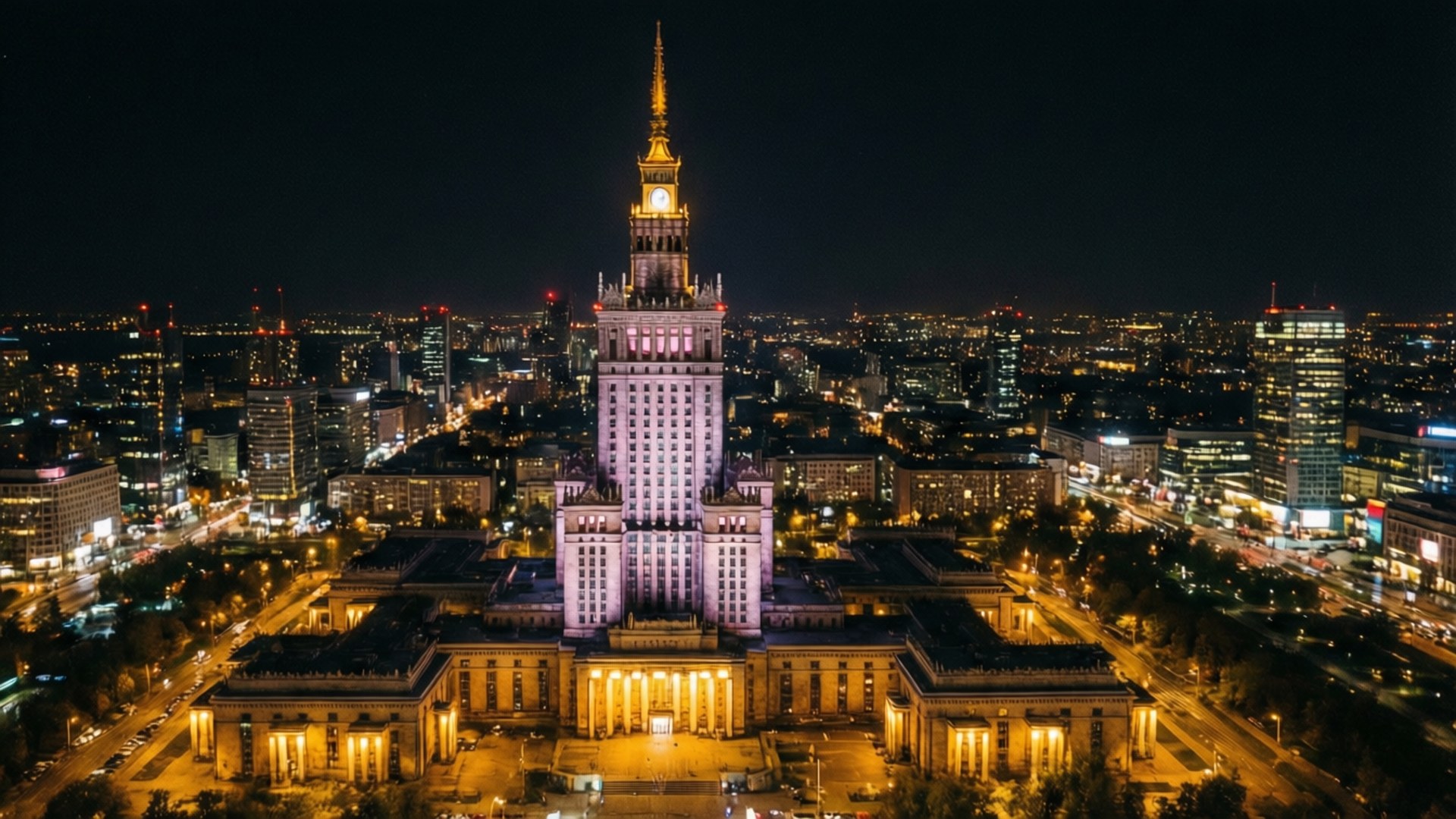 Warsaw Palace of Culture Night 壁紙 — 一座宏偉的照明塔樓建築在夜晚主導著廣闊的城市景觀，街道閃爍，遠處摩天大樓林立。