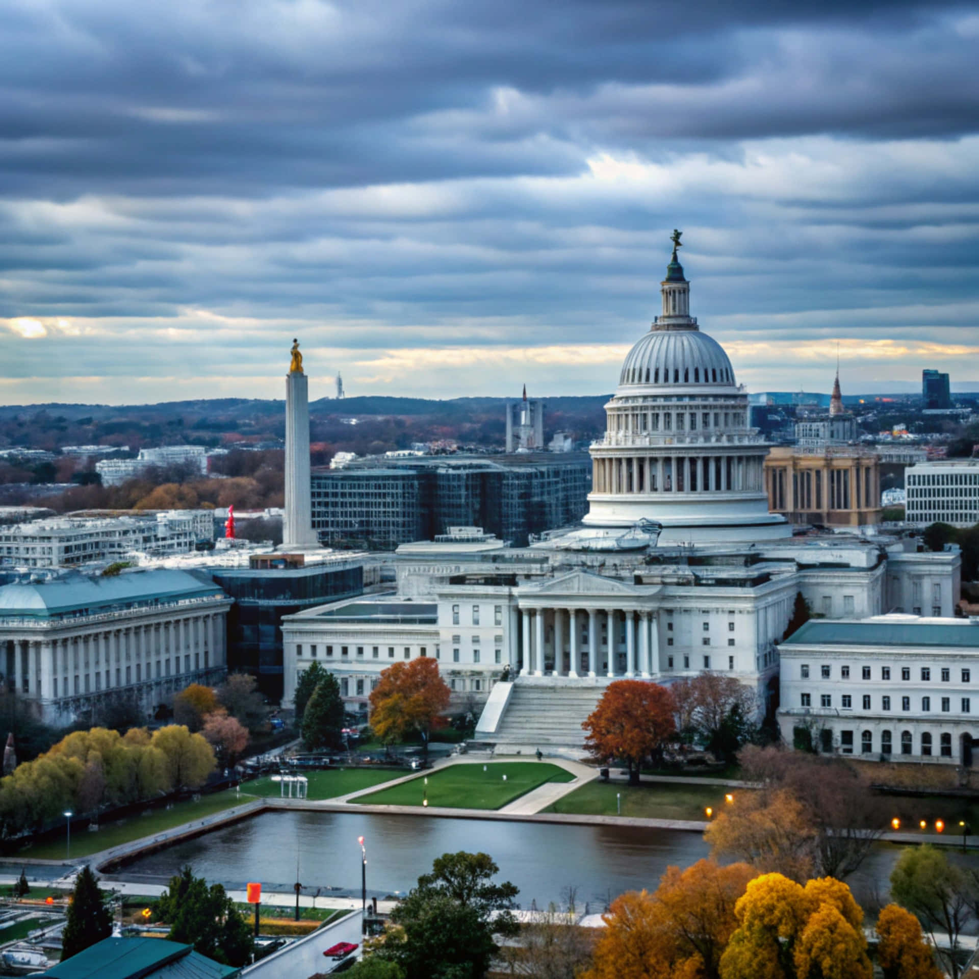 Washington Skyline 壁紙 — 美國國會大廈在戲劇性的多雲天空下巍然聳立，前景有秋樹和倒映的池塘。