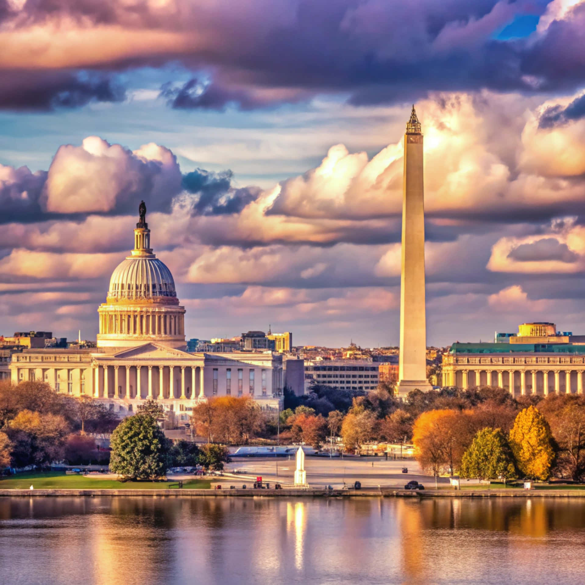 Washington Skyline 壁紙 — 美國國會大廈和華盛頓紀念碑在壯麗的日落天空下巍然聳立，雲彩倒映在潮汐湖的水面上。