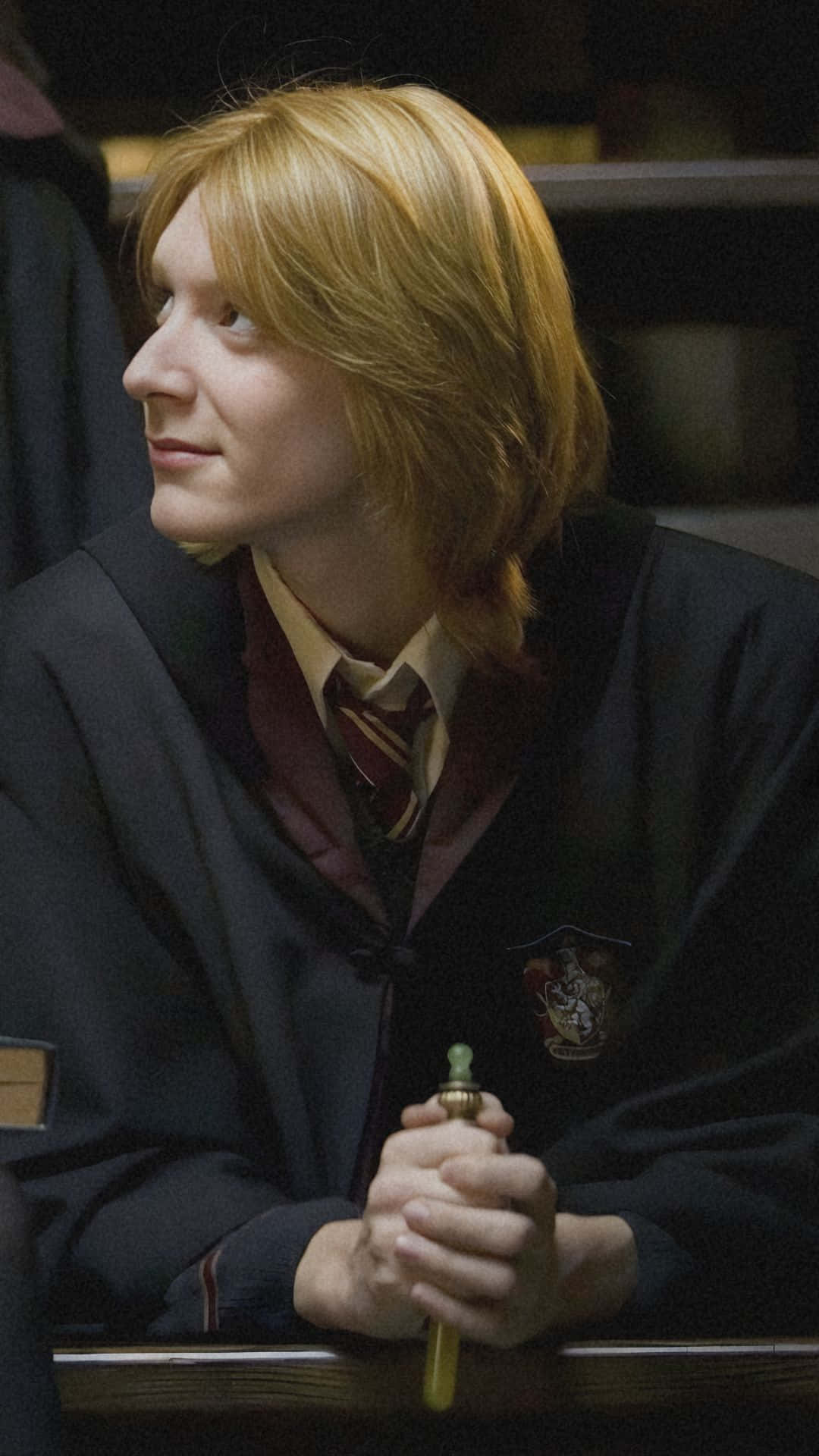  壁紙 — 一位紅髮年輕男子身穿深色長袍，在昏暗的房間裡手持魔杖，望向一旁。