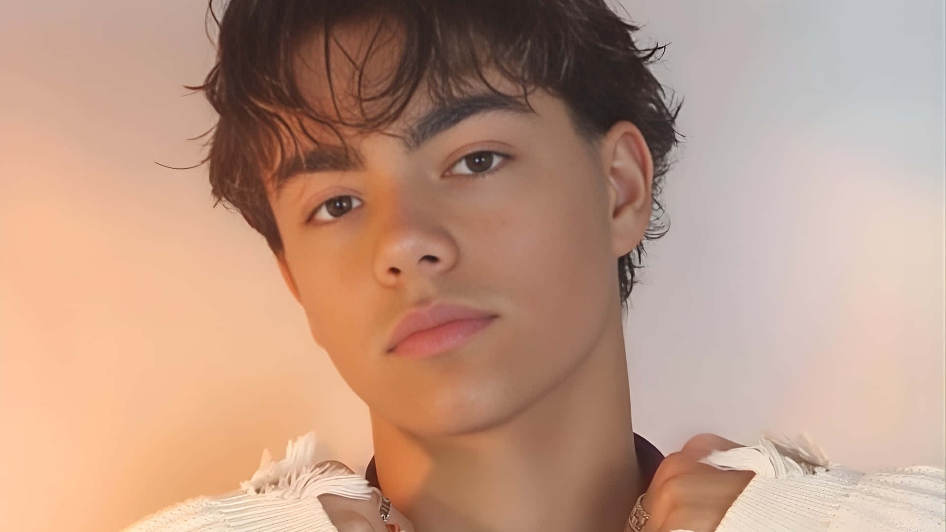  壁紙 — 一位深色亂髮的年輕男子在柔和漸變背景前直視鏡頭。