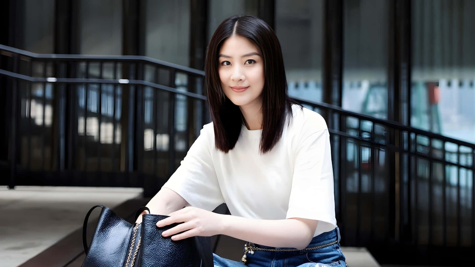  壁紙 — 一位深色頭髮的年輕女性在現代樓梯上微笑，手持黑色手袋。