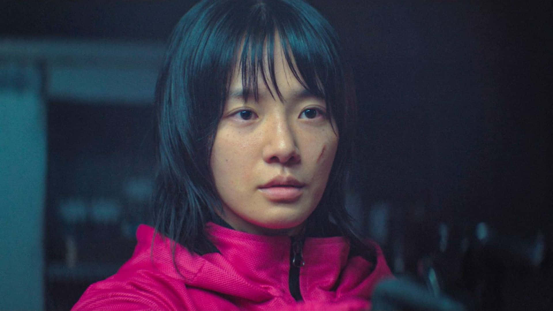  壁紙 — 一位深色頭髮、身穿粉紅色外套的年輕女子，在昏暗的藍色環境燈光房間裡專注地凝視。