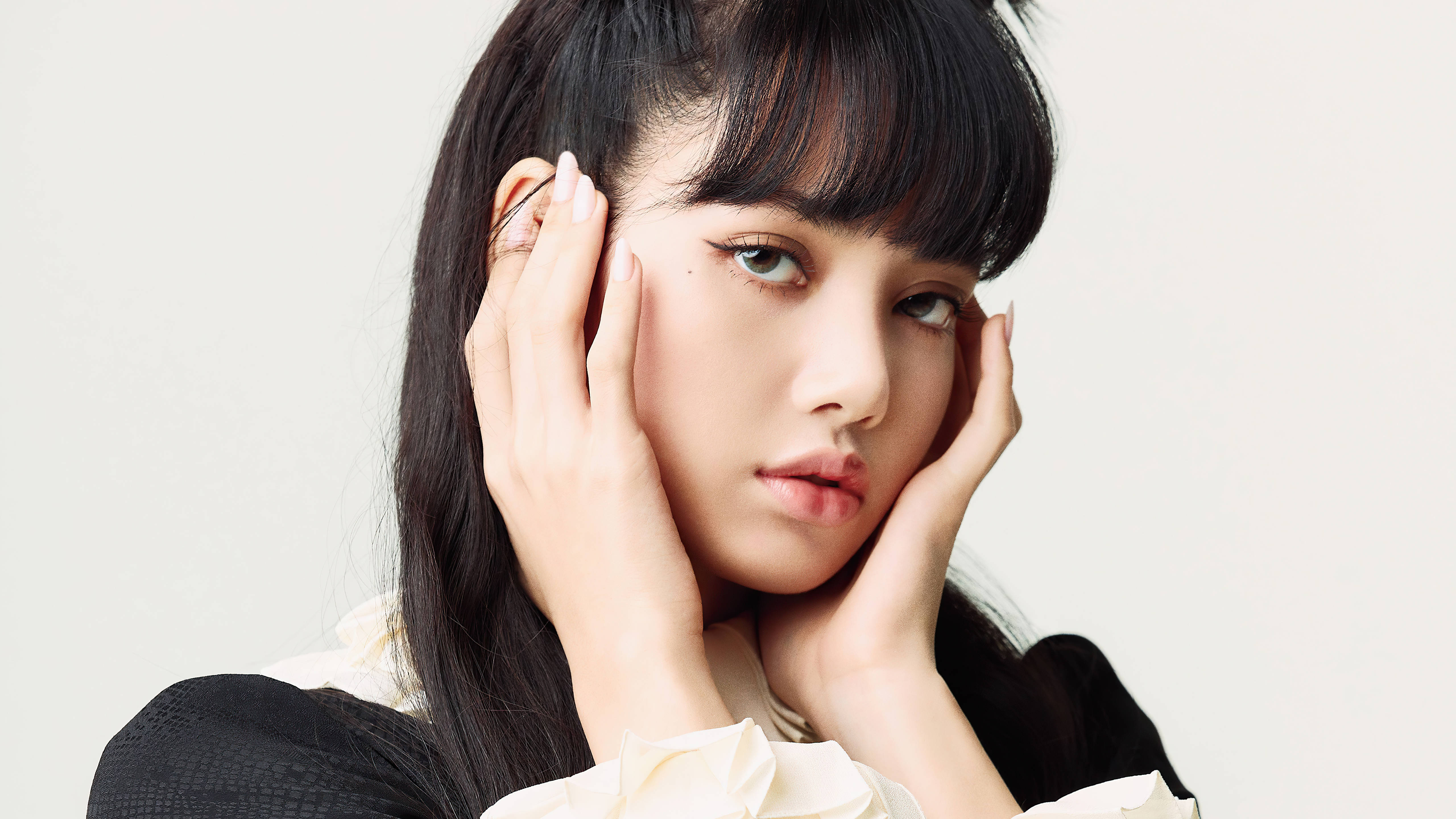 Lisa 手捧臉 BLACKPINK 桌面壁紙 壁紙 — 一位深色頭髮、有瀏海的年輕女性，在純色淺色背景前，用雙手輕輕捧著臉頰。