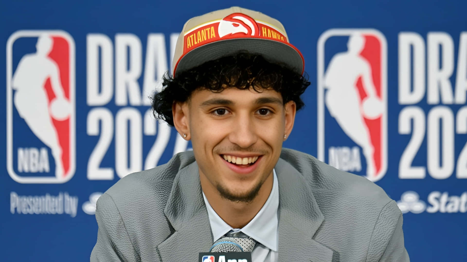 壁紙 — 一位微笑的年輕籃球運動員在2022年NBA選秀記者會上戴著亞特蘭大老鷹隊帽子。